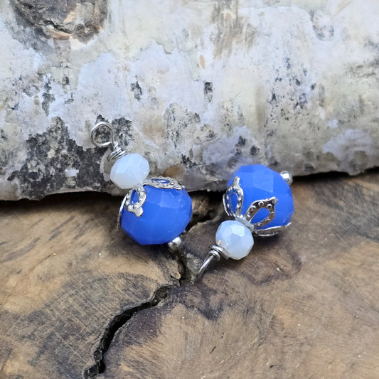 Das Bild zeigt zwei handgefertigte Anhänger mit einer blauen und einer weißen Kristallglasperle, ideal für die individuelle Schmuckherstellung.