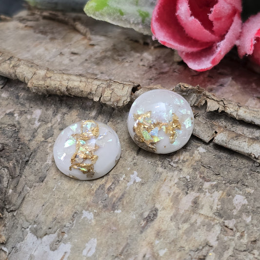 Das Bild zeigt runde Cabochons mit einem Durchmesser von 12 mm. Sie sind milchig-weiß und haben eine glatte, glänzende Oberfläche. Im Inneren der Cabochons sind feine, schimmernde Flakes eingearbeitet, die je nach Lichteinfall dezent funkeln. Die Flakes reflektieren das Licht in sanften, leicht changierenden Tönen. Die Cabochons wirken edel und leicht transparent. Sie eignen sich für die Schmuckherstellung, beispielsweise für Ringe, Anhänger oder Ohrstecker.