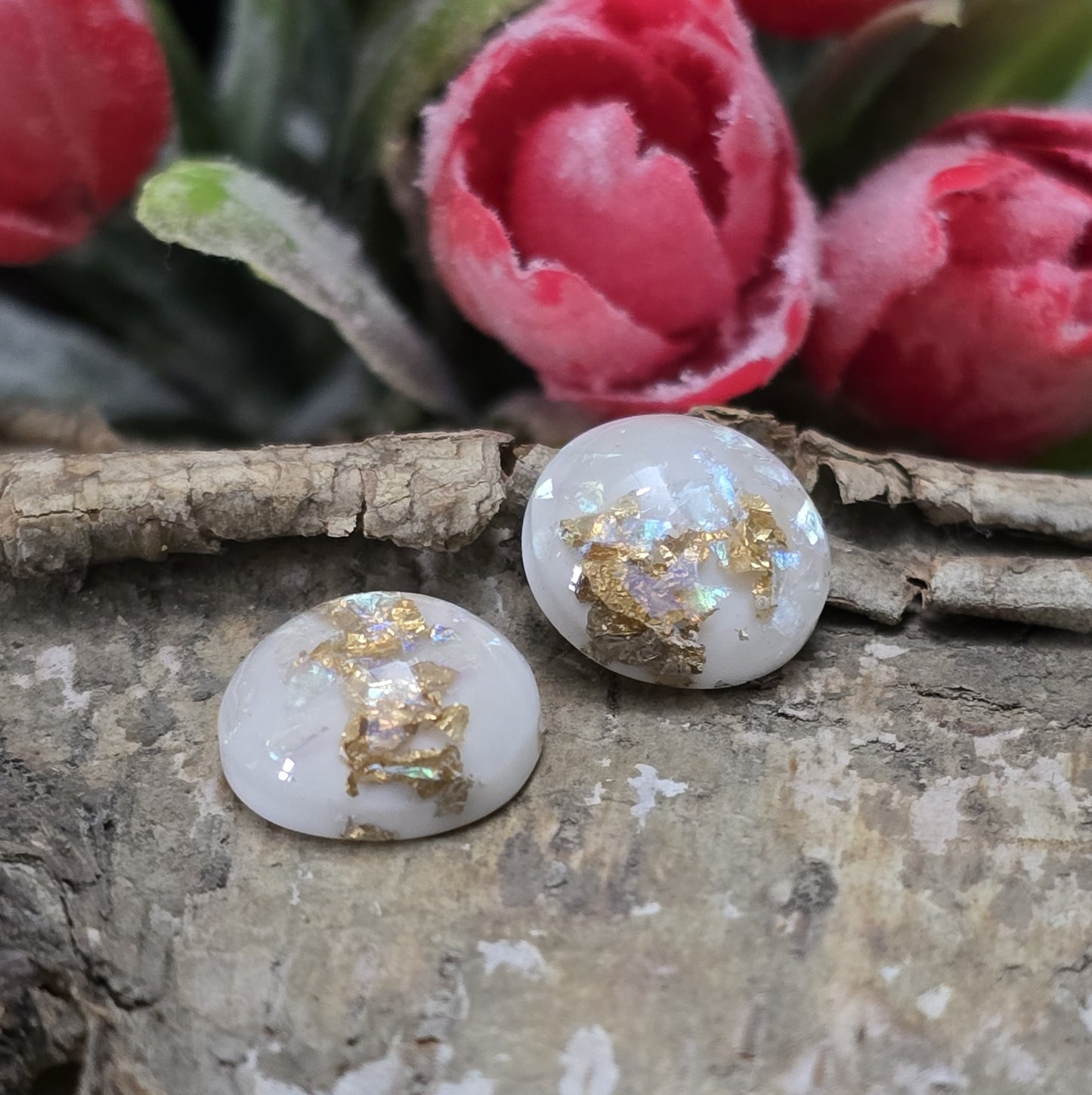 Das Bild zeigt runde Cabochons mit einem Durchmesser von 12 mm. Sie sind milchig-weiß und haben eine glatte, glänzende Oberfläche. Im Inneren der Cabochons sind feine, schimmernde Flakes eingearbeitet, die je nach Lichteinfall dezent funkeln. Die Flakes reflektieren das Licht in sanften, leicht changierenden Tönen. Die Cabochons wirken edel und leicht transparent. Sie eignen sich für die Schmuckherstellung, beispielsweise für Ringe, Anhänger oder Ohrstecker.