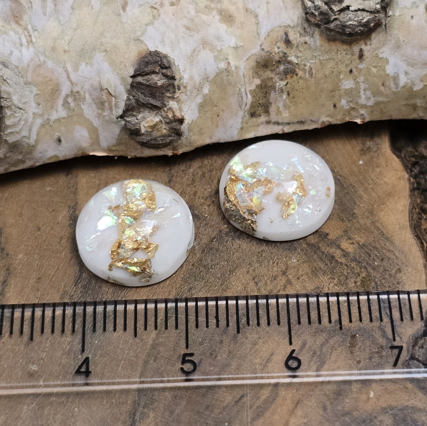 Das Bild zeigt runde Cabochons mit einem Durchmesser von 12 mm. Sie sind milchig-weiß und haben eine glatte, glänzende Oberfläche. Im Inneren der Cabochons sind feine, schimmernde Flakes eingearbeitet, die je nach Lichteinfall dezent funkeln. Die Flakes reflektieren das Licht in sanften, leicht changierenden Tönen. Die Cabochons wirken edel und leicht transparent. Sie eignen sich für die Schmuckherstellung, beispielsweise für Ringe, Anhänger oder Ohrstecker.