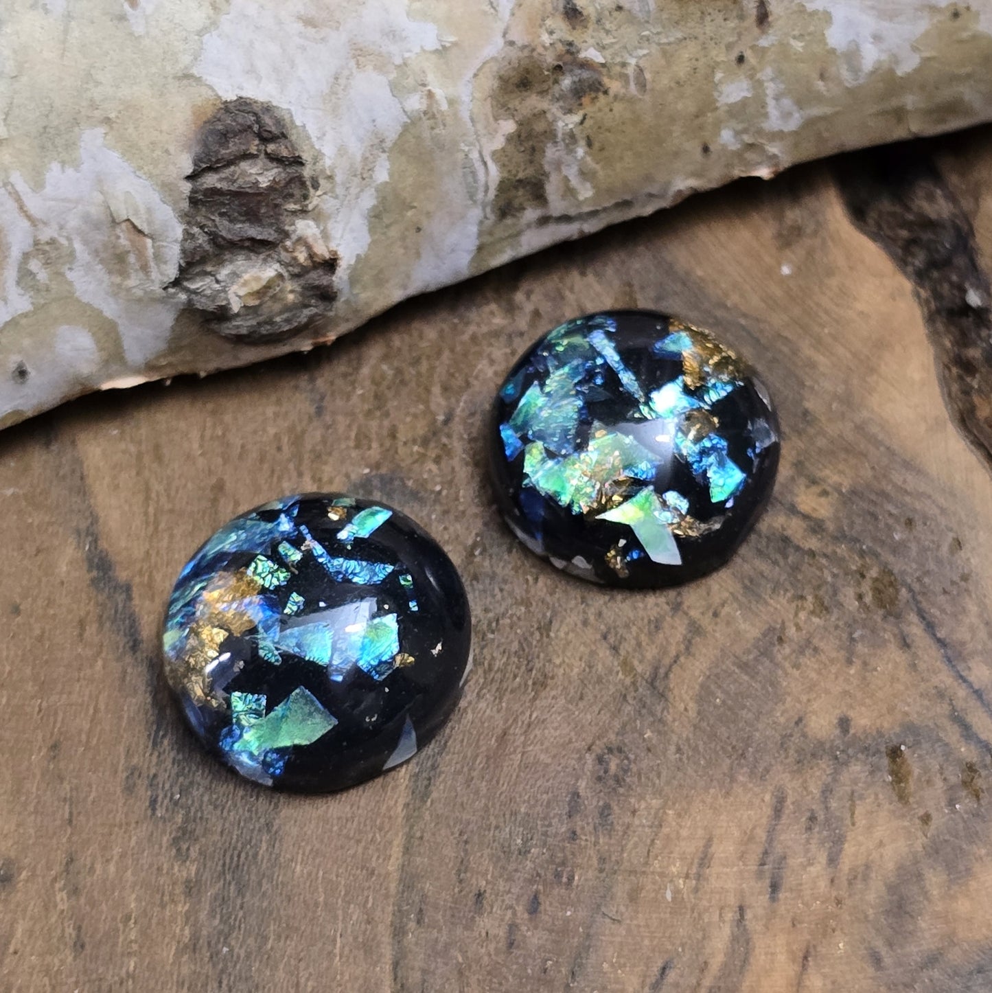 Das Bild zeigt vier runde Cabochons mit einem Durchmesser von 12 mm. Sie sind tiefschwarz und haben eine glatte, glänzende Oberfläche. Im Inneren der Cabochons befinden sich feine, schimmernde Flakes, die je nach Lichteinfall dezent funkeln. Die Flakes erzeugen kleine, reflektierende Lichtpunkte, die dem Schwarz eine besondere Tiefe verleihen. Die Cabochons wirken edel und modern. Sie eignen sich für die Schmuckherstellung, beispielsweise für Ringe, Anhänger oder Ohrstecker.