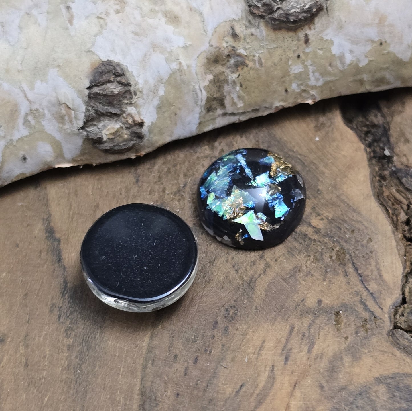 Das Bild zeigt vier runde Cabochons mit einem Durchmesser von 12 mm. Sie sind tiefschwarz und haben eine glatte, glänzende Oberfläche. Im Inneren der Cabochons befinden sich feine, schimmernde Flakes, die je nach Lichteinfall dezent funkeln. Die Flakes erzeugen kleine, reflektierende Lichtpunkte, die dem Schwarz eine besondere Tiefe verleihen. Die Cabochons wirken edel und modern. Sie eignen sich für die Schmuckherstellung, beispielsweise für Ringe, Anhänger oder Ohrstecker.