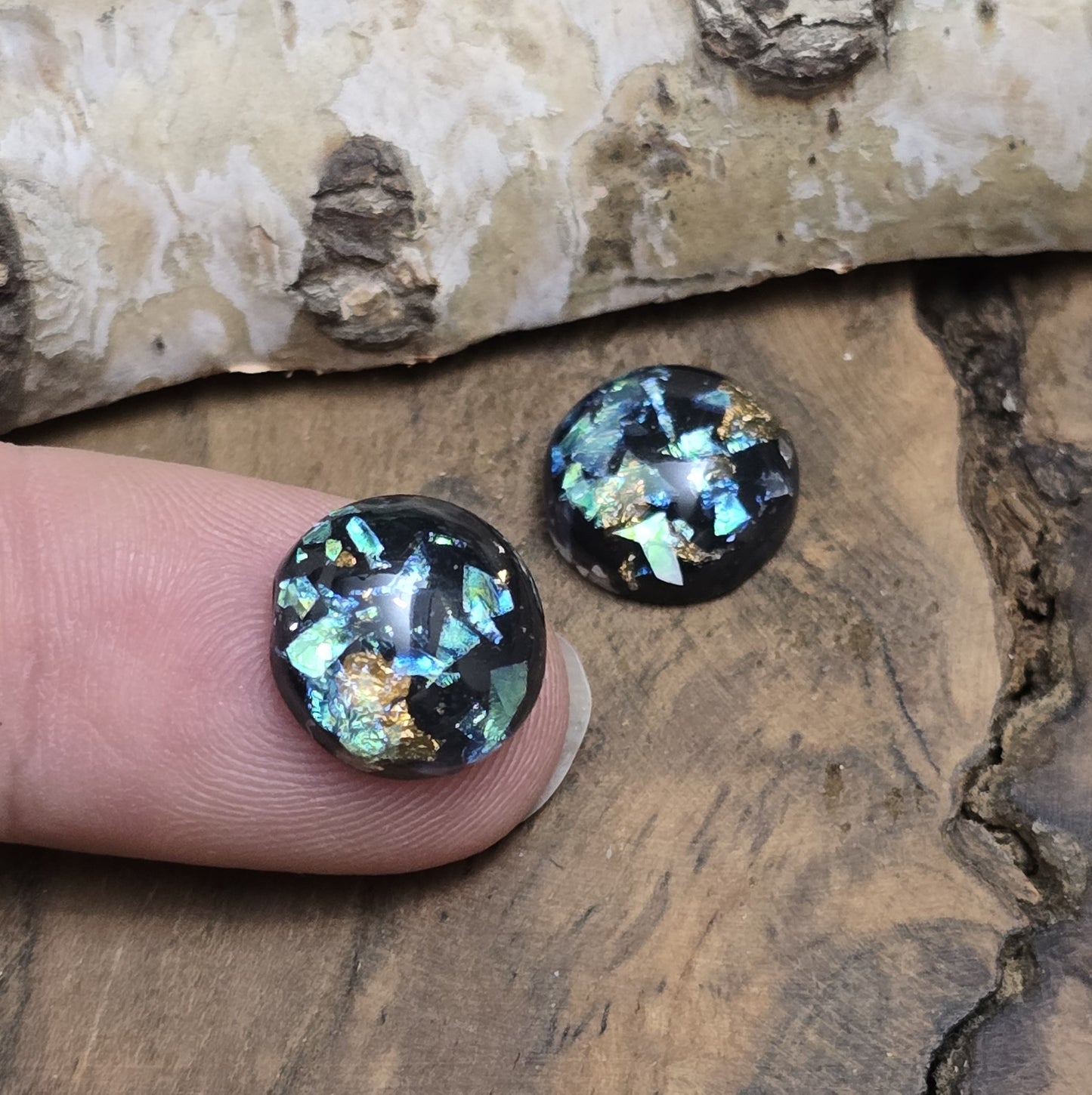 Das Bild zeigt vier runde Cabochons mit einem Durchmesser von 12 mm. Sie sind tiefschwarz und haben eine glatte, glänzende Oberfläche. Im Inneren der Cabochons befinden sich feine, schimmernde Flakes, die je nach Lichteinfall dezent funkeln. Die Flakes erzeugen kleine, reflektierende Lichtpunkte, die dem Schwarz eine besondere Tiefe verleihen. Die Cabochons wirken edel und modern. Sie eignen sich für die Schmuckherstellung, beispielsweise für Ringe, Anhänger oder Ohrstecker.