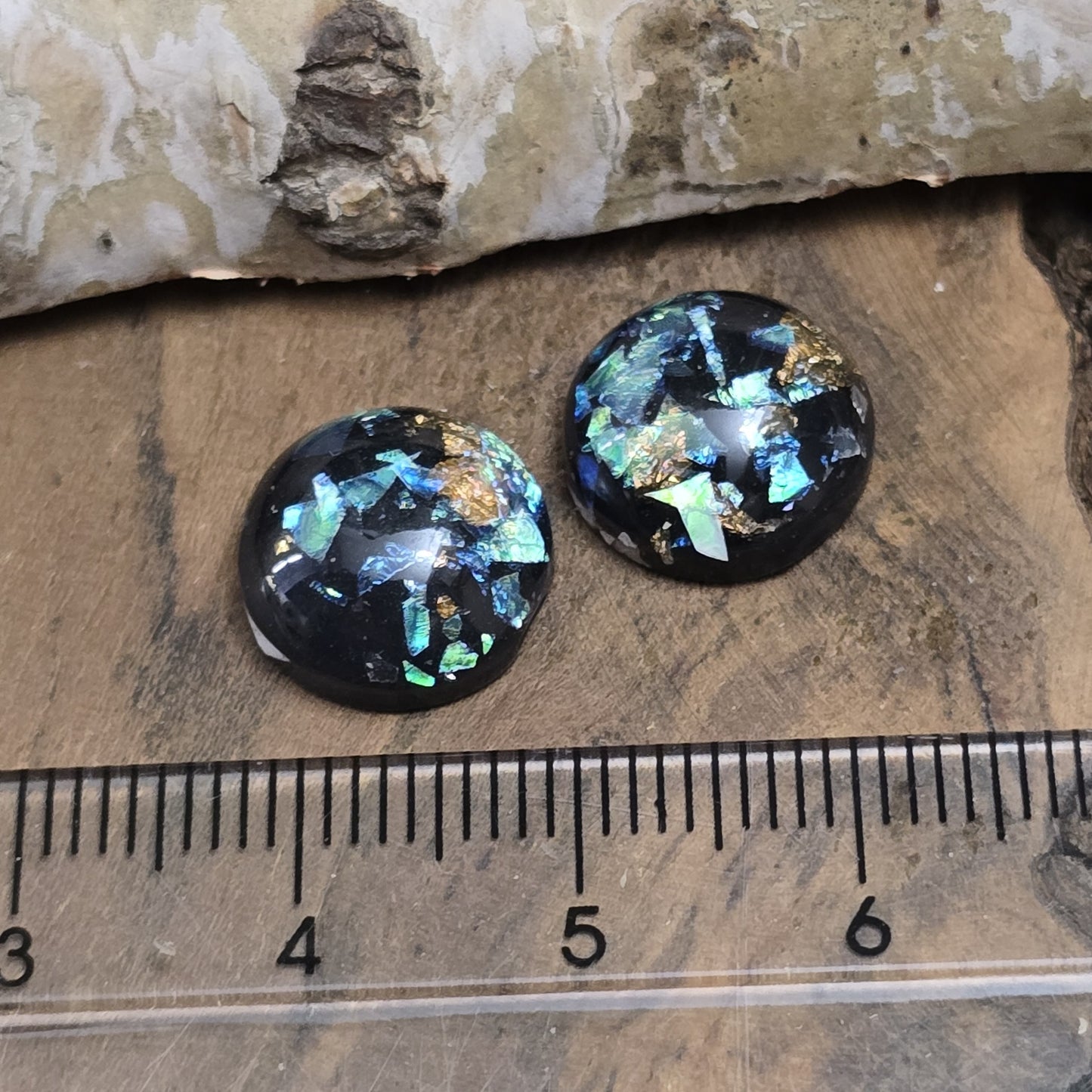 Das Bild zeigt vier runde Cabochons mit einem Durchmesser von 12 mm. Sie sind tiefschwarz und haben eine glatte, glänzende Oberfläche. Im Inneren der Cabochons befinden sich feine, schimmernde Flakes, die je nach Lichteinfall dezent funkeln. Die Flakes erzeugen kleine, reflektierende Lichtpunkte, die dem Schwarz eine besondere Tiefe verleihen. Die Cabochons wirken edel und modern. Sie eignen sich für die Schmuckherstellung, beispielsweise für Ringe, Anhänger oder Ohrstecker.
