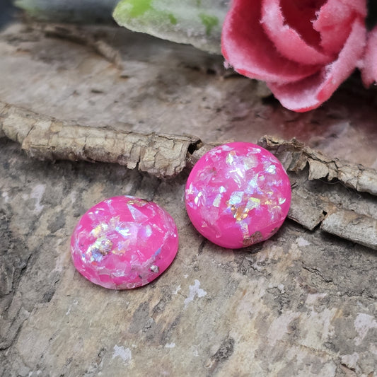 Das Bild zeigt runde Cabochons mit einem Durchmesser von 12 mm. Sie sind in einem kräftigen Pinkton gehalten und haben eine glatte, glänzende Oberfläche. Im Inneren befinden sich schimmernde Flakes, die das Licht reflektieren und für funkelnde Akzente sorgen. Je nach Lichteinfall changieren die Flakes und verleihen den Cabochons eine edle, lebendige Optik. Sie eignen sich perfekt für die Schmuckherstellung, beispielsweise für Ringe, Anhänger oder Ohrstecker.