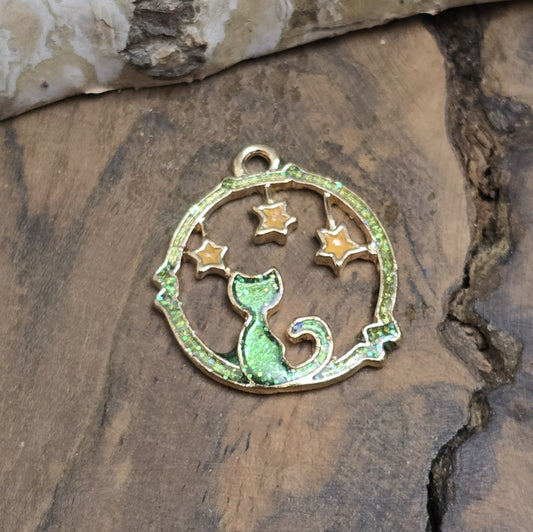 Das Bild zeigt einen goldfarbenen Anhänger mit einer Katze. Die Katzenfigur ist mit glitzerndem grünen Resin verziert, der bei Lichteinfall funkelt. Kleine gelbe Sterne zieren den Himmel über ihr und verleihen dem Anhänger eine magische Note. Die goldfarbige Umrandung gibt dem Design einen edlen Rahmen. Die Anhänger haben eine Länge von 21mm und eignen sich für Schmuckherstellung oder kreative Accessoires.