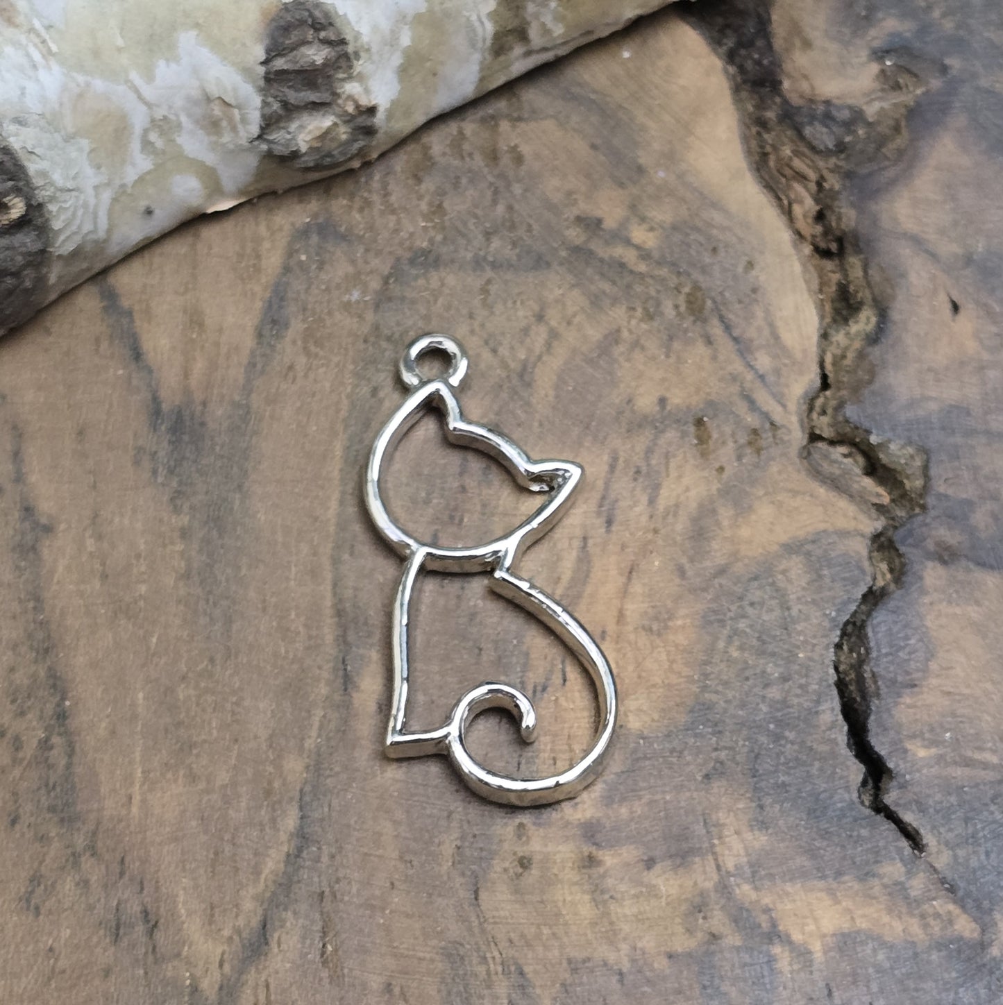 Das Bild zeigt einen filigranen Anhänger in Katzenform. Die Anhänger sind silberfarben und zeichnen sich durch ein zartes, detailliertes Design aus. Die Katzen sind elegant und geschwungen, mit feinen Linien und einer klaren, minimalistischen Form. Die Anhänger haben eine Größe von ca. 25mm und eignen sich perfekt für die Schmuckherstellung oder als dekorative Accessoires.