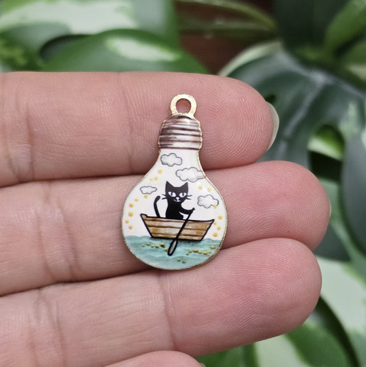 Das Bild zeigt einen goldfarbenen Anhänger in Glühbirnenform, auf dem ein Katzenmotiv abgebildet ist. Eine Katze sitzt in einem Ruderboot und fährt auf einem malerischen See. Das filigrane Design ist von einer goldenen Umrandung eingefasst, die dem Anhänger eine edle Note verleiht. Der Anhänger hat eine Größe von 27mm und eignet sich hervorragend für Schmuckherstellung oder DIY-Projekte.