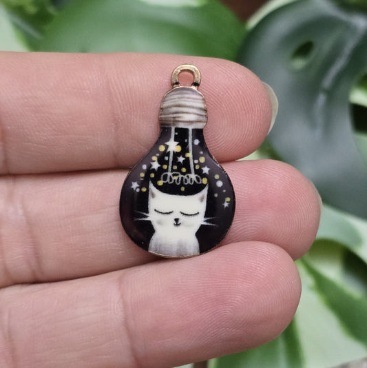 Das Bild zeigt einen goldfarbenen Anhänger in Glühbirnenform, auf dem eine weiße Katze mit geschlossenen Augen abgebildet ist. Die Katze ist nur zur Hälfte sichtbar und sitzt auf einem schwarzen Hintergrund, der die Eleganz des Designs unterstreicht. Der Anhänger hat eine Größe von 27mm und ist von einer goldenen Umrandung eingefasst, die ihm eine edle Ausstrahlung verleiht. Dieser Anhänger eignet sich hervorragend für Schmuckherstellung und kreative DIY-Projekte.