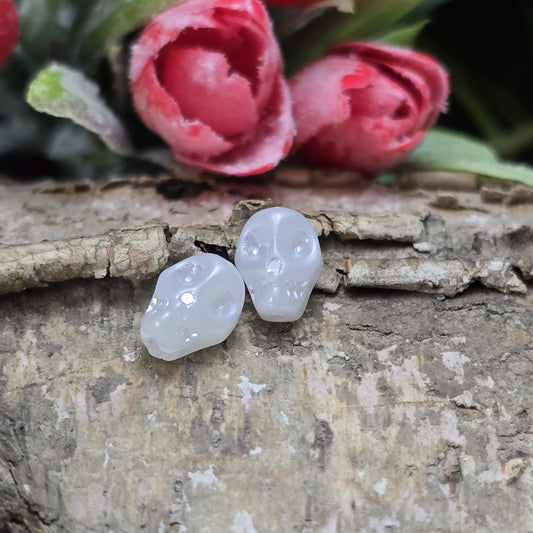 Das Bild zeigt zwei matt weiße Glasperlen in Totenkopf-Form. Die Perlen sind dreidimensional gestaltet, sodass die Schädelstruktur mit Augenhöhlen, Nase und Kiefer erkennbar ist. Die Bohrung verläuft von oben nach unten, sodass sie ideal für Schmuckprojekte verwendet werden können. Durch die matte Oberfläche wirkt das Design besonders stilvoll und modern.