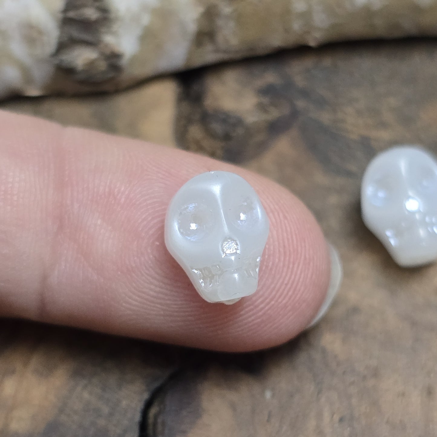 Das Bild zeigt zwei matt weiße Glasperlen in Totenkopf-Form. Die Perlen sind dreidimensional gestaltet, sodass die Schädelstruktur mit Augenhöhlen, Nase und Kiefer erkennbar ist. Die Bohrung verläuft von oben nach unten, sodass sie ideal für Schmuckprojekte verwendet werden können. Durch die matte Oberfläche wirkt das Design besonders stilvoll und modern.
