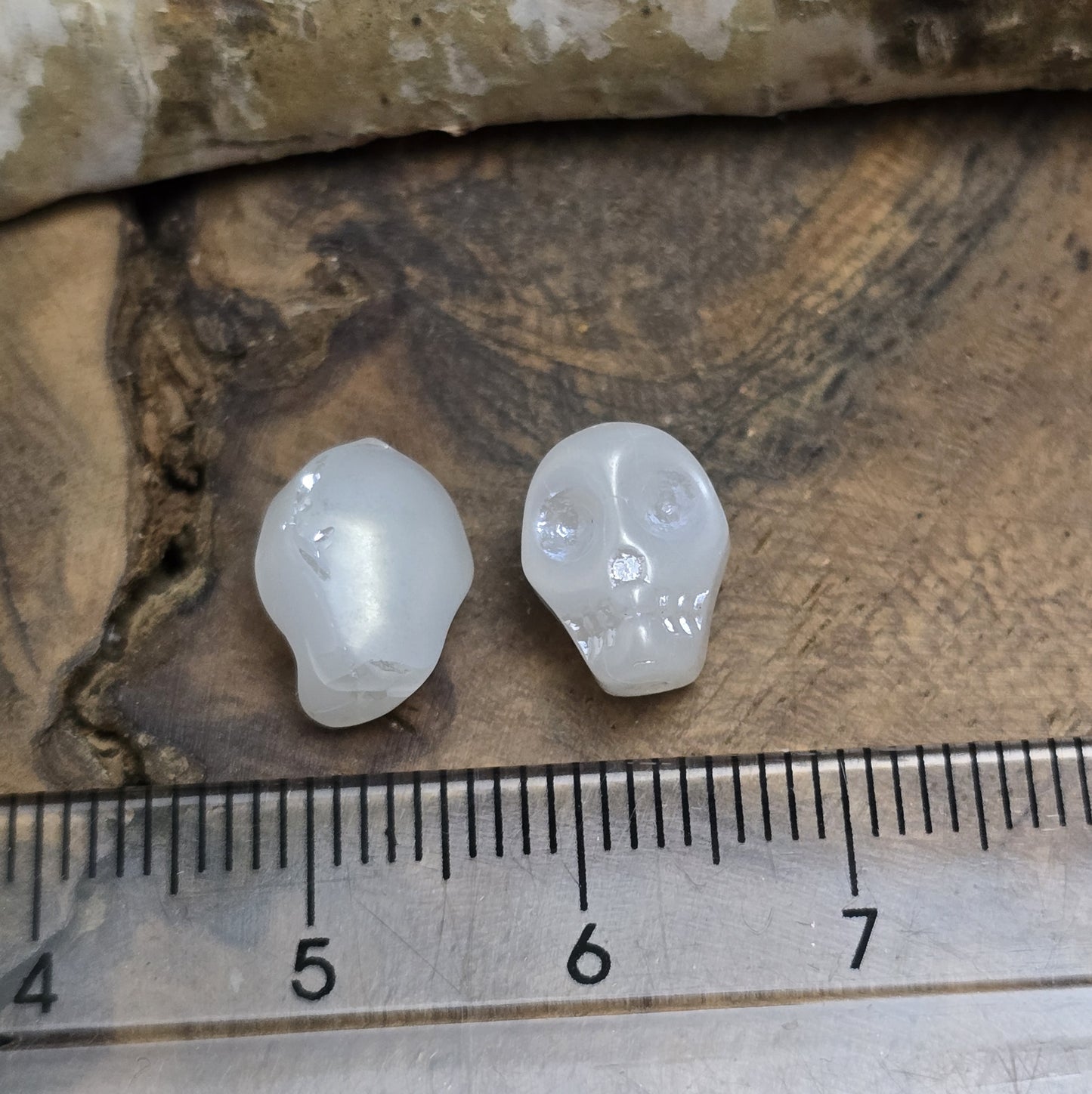 Das Bild zeigt zwei matt weiße Glasperlen in Totenkopf-Form. Die Perlen sind dreidimensional gestaltet, sodass die Schädelstruktur mit Augenhöhlen, Nase und Kiefer erkennbar ist. Die Bohrung verläuft von oben nach unten, sodass sie ideal für Schmuckprojekte verwendet werden können. Durch die matte Oberfläche wirkt das Design besonders stilvoll und modern.
