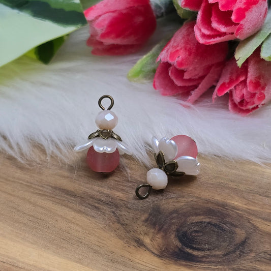 Das Bild zeigt zwei handgefertigte Anhänger mit einer matten lachsfarbenen Glasperle als Hauptakzent. Zarte rosa Kristallglasperlen verleihen dem Design einen sanften Schimmer, während perlweiße Blütenkäppchen aus Acryl und antik bronzefarbene Perlenkappen den Anhängern eine nostalgische, elegante Note geben. Mit einer Größe von ca. 20mm sind sie perfekt für romantische Schmuckkreationen.