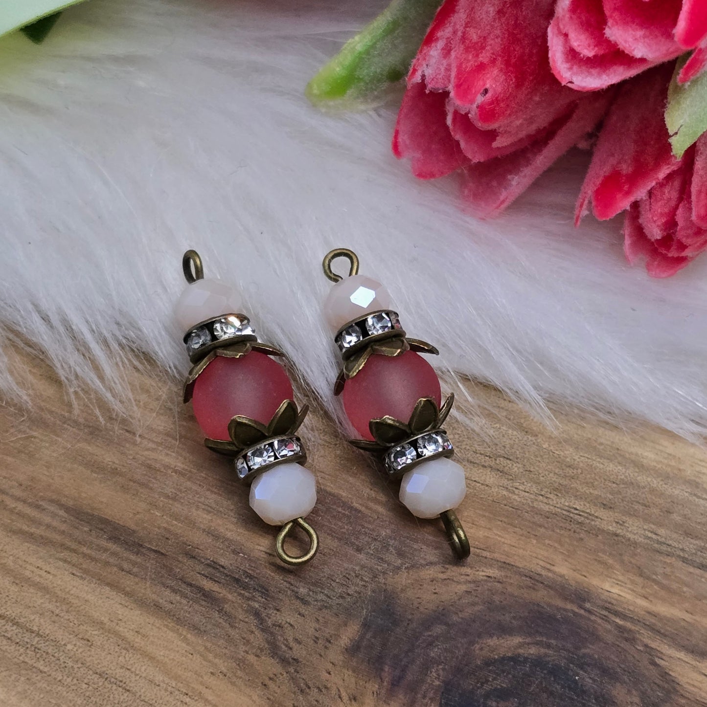 Das Bild zeigt zwei handgefertigte Verbinder im Shabby-Stil, die aus matten, transparenten Glasperlen in Lachs und schimmernden beige Kristallglasperlen gefertigt sind. Strassrondelle setzen funkelnde Akzente, während antik bronzefarbige Metallelemente den nostalgischen Look unterstreichen. Die Verbinder haben eine Länge von ca. 30mm und eignen sich ideal für Schmuckkreationen wie Armbänder oder Ketten.
