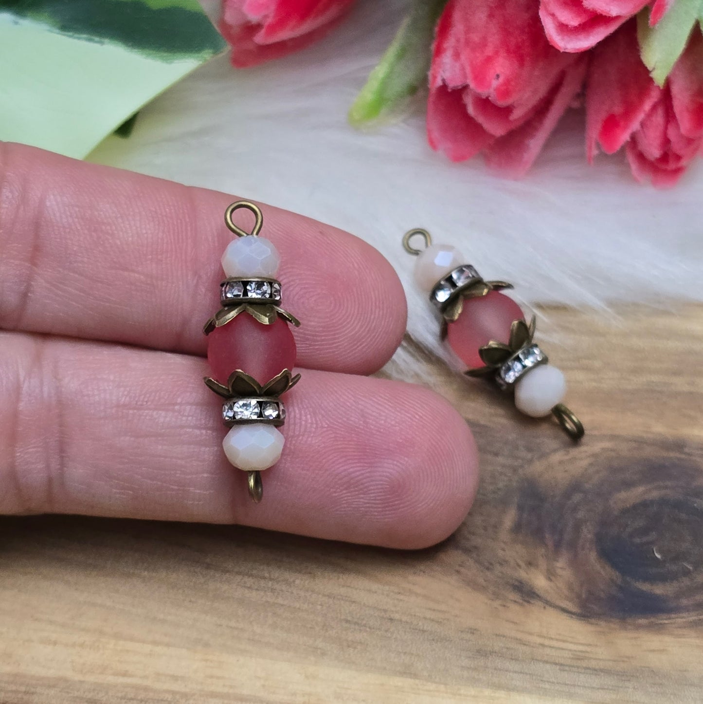 Das Bild zeigt zwei handgefertigte Verbinder im Shabby-Stil, die aus matten, transparenten Glasperlen in Lachs und schimmernden beige Kristallglasperlen gefertigt sind. Strassrondelle setzen funkelnde Akzente, während antik bronzefarbige Metallelemente den nostalgischen Look unterstreichen. Die Verbinder haben eine Länge von ca. 30mm und eignen sich ideal für Schmuckkreationen wie Armbänder oder Ketten.
