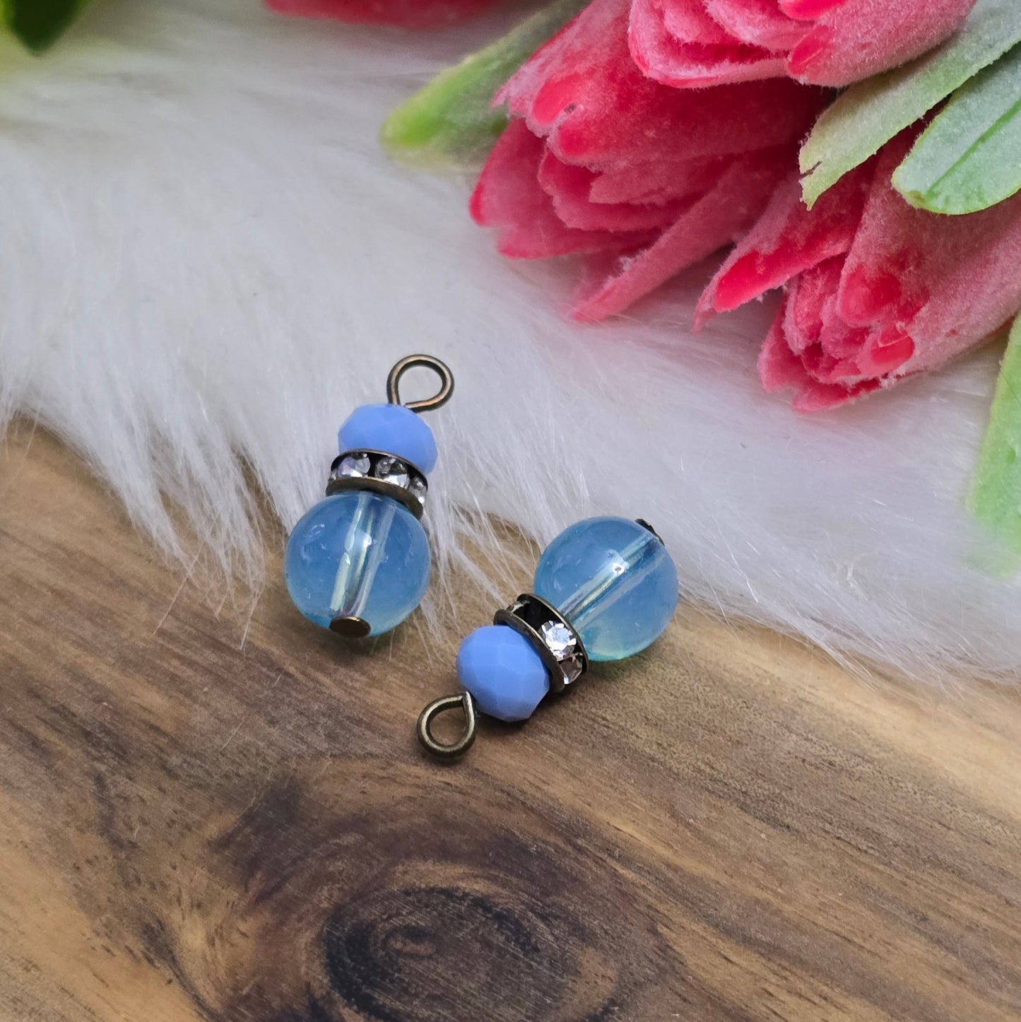 Das Bild zeigt zwei handgefertigte Anhänger mit einer Kombination aus transparenten hellblauen Glasperlen und opaken hellblauen Kristallglasperlen. Ein funkelndes Strassrondell setzt glitzernde Akzente, während antik bronzefarbige Metallelemente dem Design einen charmanten Vintage-Touch verleihen. Die filigranen Details und die harmonische Farbzusammenstellung machen die Anhänger zu einem stilvollen Blickfang für Schmuckkreationen.