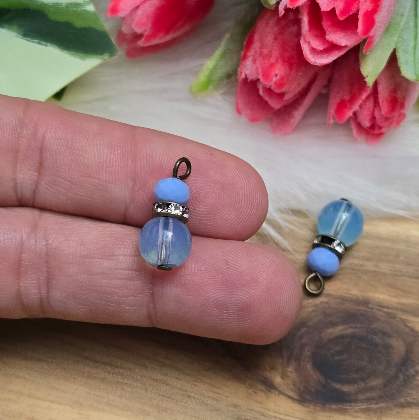 Das Bild zeigt zwei handgefertigte Anhänger mit einer Kombination aus transparenten hellblauen Glasperlen und opaken hellblauen Kristallglasperlen. Ein funkelndes Strassrondell setzt glitzernde Akzente, während antik bronzefarbige Metallelemente dem Design einen charmanten Vintage-Touch verleihen. Die filigranen Details und die harmonische Farbzusammenstellung machen die Anhänger zu einem stilvollen Blickfang für Schmuckkreationen.