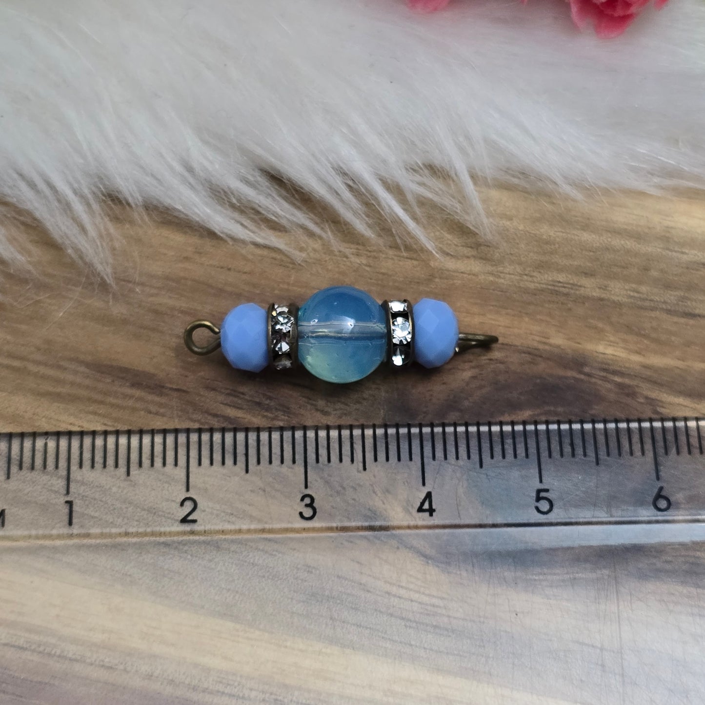 Das Bild zeigt zwei handgefertigte Verbinder mit hellblauen Glasperlen. Die Kombination aus einer transparenten hellblauen Glasperle (8mm) und einer opaken hellblauen Kristallglasperle wird durch ein funkelndes Strassrondell ergänzt. Antik bronzefarbene Metallelemente verleihen den Verbindern einen eleganten Vintage-Look. Mit einer Länge von 27mm sind sie ideal für die Schmuckherstellung.