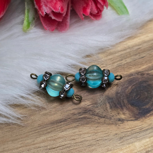 Das Bild zeigt zwei handgefertigte Verbinder mit mintfarbenen Glasperlen in Kürbisform und facettierten Kristallglasperlen. Strassrondelle sorgen für funkelnde Akzente, während antik bronzefarbene Metallelemente dem Design einen eleganten Vintage-Charme verleihen. Die Verbinder sind ca. 25mm groß und ideal für Schmuckkreationen.