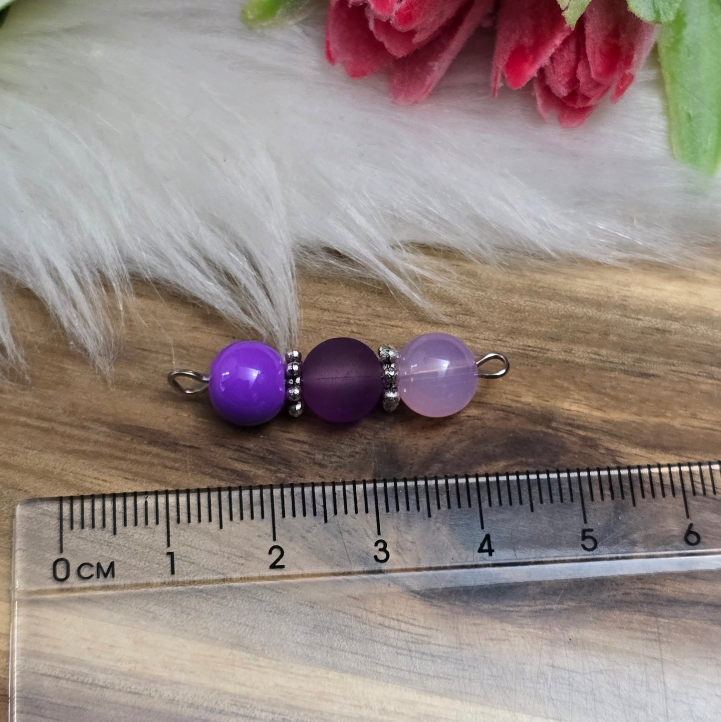 Das Bild zeigt zwei handgefertigte Verbinder mit lila und violetten Glasperlen in unterschiedlichen Ausführungen – eine opake, eine matte und eine milchig transparente. Die Perlen sind harmonisch angeordnet und werden von detailreich verzierten, antik-silberfarbenen Metallelementen eingefasst. Die filigranen Zwischenelemente verleihen den Verbindern eine edle Vintage-Optik. Mit einer Länge von ca. 33mm eignen sie sich perfekt für kreative Schmuckdesigns wie Armbänder, Ketten oder Ohrringe.