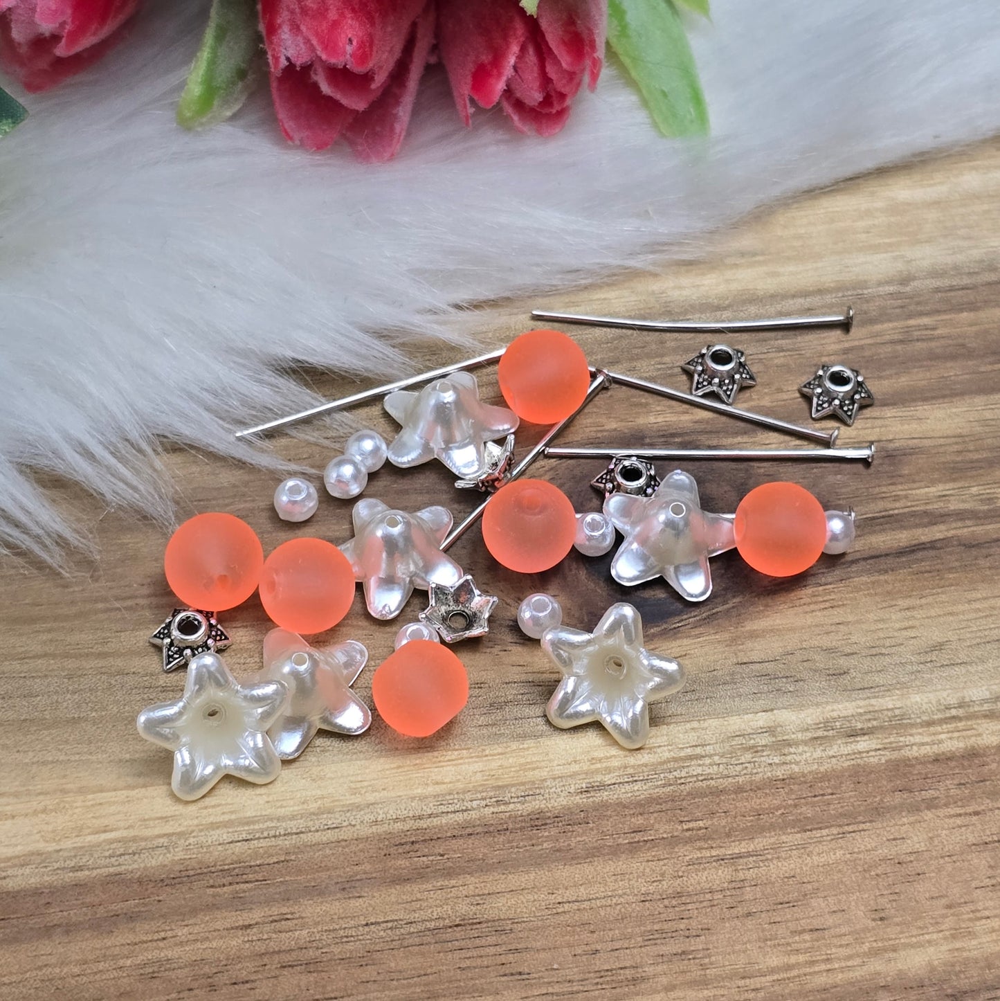 Das Bild zeigt ein 30-teiliges Bastelset zur Schmuckherstellung, ideal für kreative Bastler. In dem Set sind Materialien enthalten, um 6 Blumenanhänger in Orange und Weiß zu gestalten. Zu sehen sind verschiedene Komponenten: matte orangefarbene Glasperlen, cremeweiße Acrylperlen, weiße Blütenkäppchen und antik silberfarbige Sternkäppchen. Alle Teile sind sorgfältig angeordnet, um die Vielseitigkeit und Farbpalette des Sets hervorzuheben. Dieses Set bietet die perfekte Grundlage für die Gestaltung einzigarti