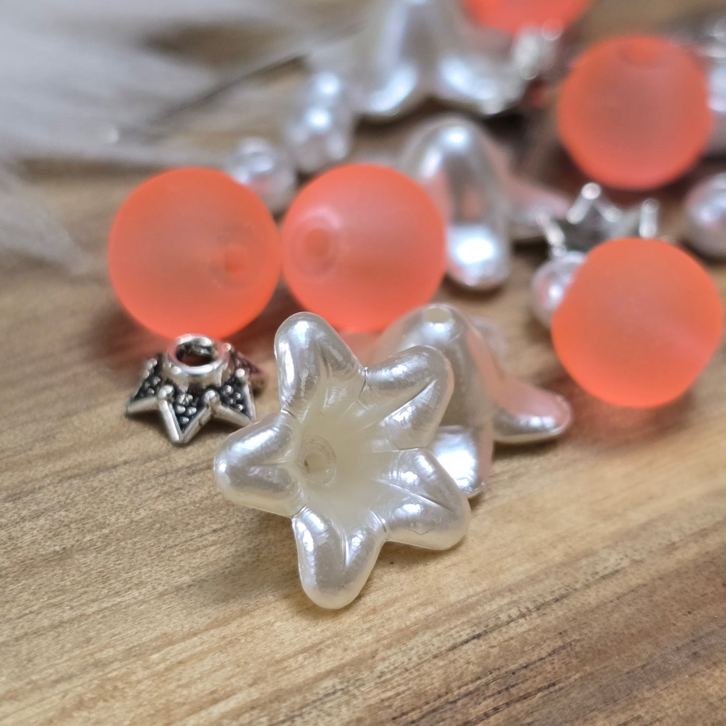 Das Bild zeigt ein 30-teiliges Bastelset zur Schmuckherstellung, ideal für kreative Bastler. In dem Set sind Materialien enthalten, um 6 Blumenanhänger in Orange und Weiß zu gestalten. Zu sehen sind verschiedene Komponenten: matte orangefarbene Glasperlen, cremeweiße Acrylperlen, weiße Blütenkäppchen und antik silberfarbige Sternkäppchen. Alle Teile sind sorgfältig angeordnet, um die Vielseitigkeit und Farbpalette des Sets hervorzuheben. Dieses Set bietet die perfekte Grundlage für die Gestaltung einzigarti