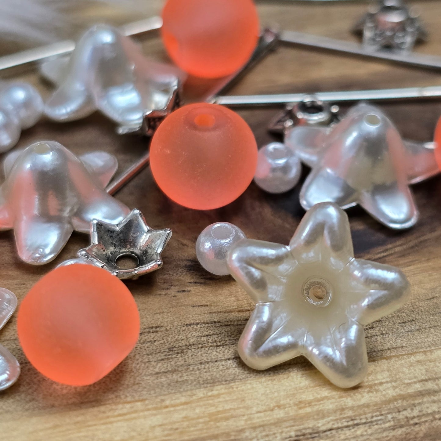 Das Bild zeigt ein 30-teiliges Bastelset zur Schmuckherstellung, ideal für kreative Bastler. In dem Set sind Materialien enthalten, um 6 Blumenanhänger in Orange und Weiß zu gestalten. Zu sehen sind verschiedene Komponenten: matte orangefarbene Glasperlen, cremeweiße Acrylperlen, weiße Blütenkäppchen und antik silberfarbige Sternkäppchen. Alle Teile sind sorgfältig angeordnet, um die Vielseitigkeit und Farbpalette des Sets hervorzuheben. Dieses Set bietet die perfekte Grundlage für die Gestaltung einzigarti