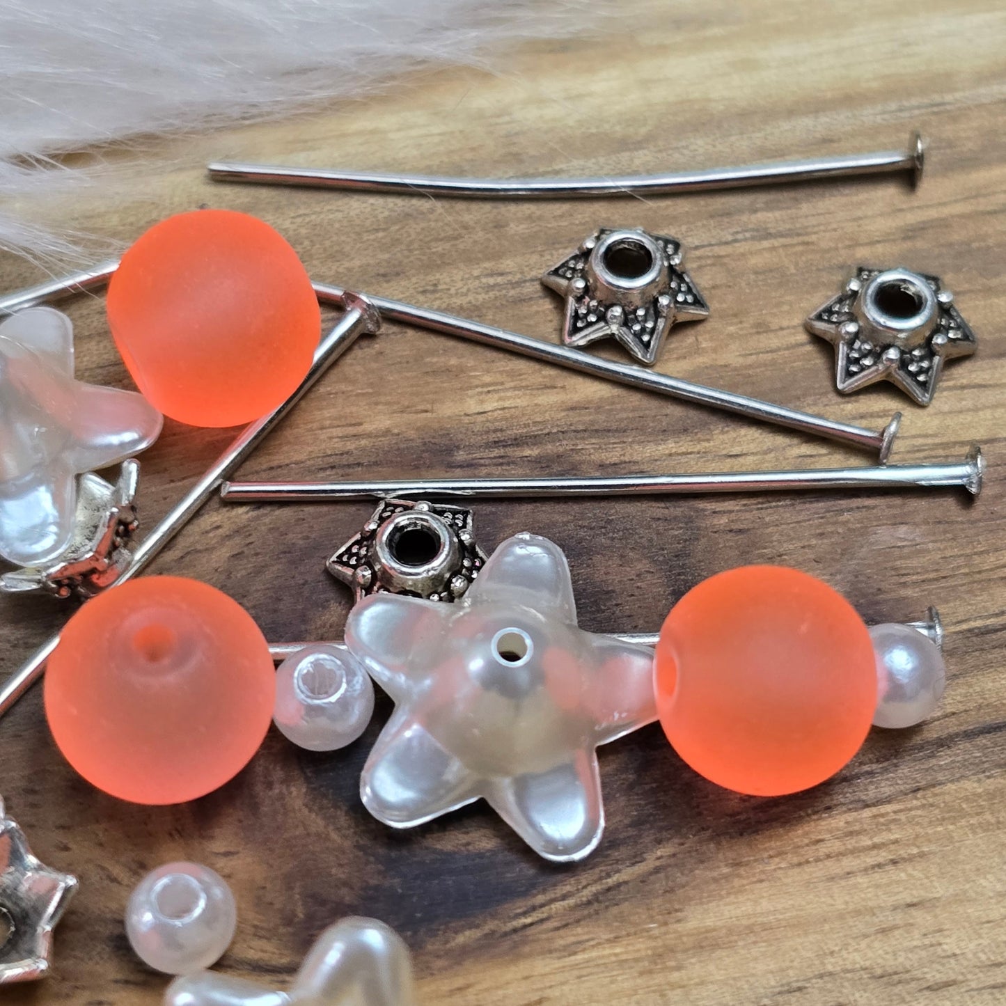 Das Bild zeigt ein 30-teiliges Bastelset zur Schmuckherstellung, ideal für kreative Bastler. In dem Set sind Materialien enthalten, um 6 Blumenanhänger in Orange und Weiß zu gestalten. Zu sehen sind verschiedene Komponenten: matte orangefarbene Glasperlen, cremeweiße Acrylperlen, weiße Blütenkäppchen und antik silberfarbige Sternkäppchen. Alle Teile sind sorgfältig angeordnet, um die Vielseitigkeit und Farbpalette des Sets hervorzuheben. Dieses Set bietet die perfekte Grundlage für die Gestaltung einzigarti