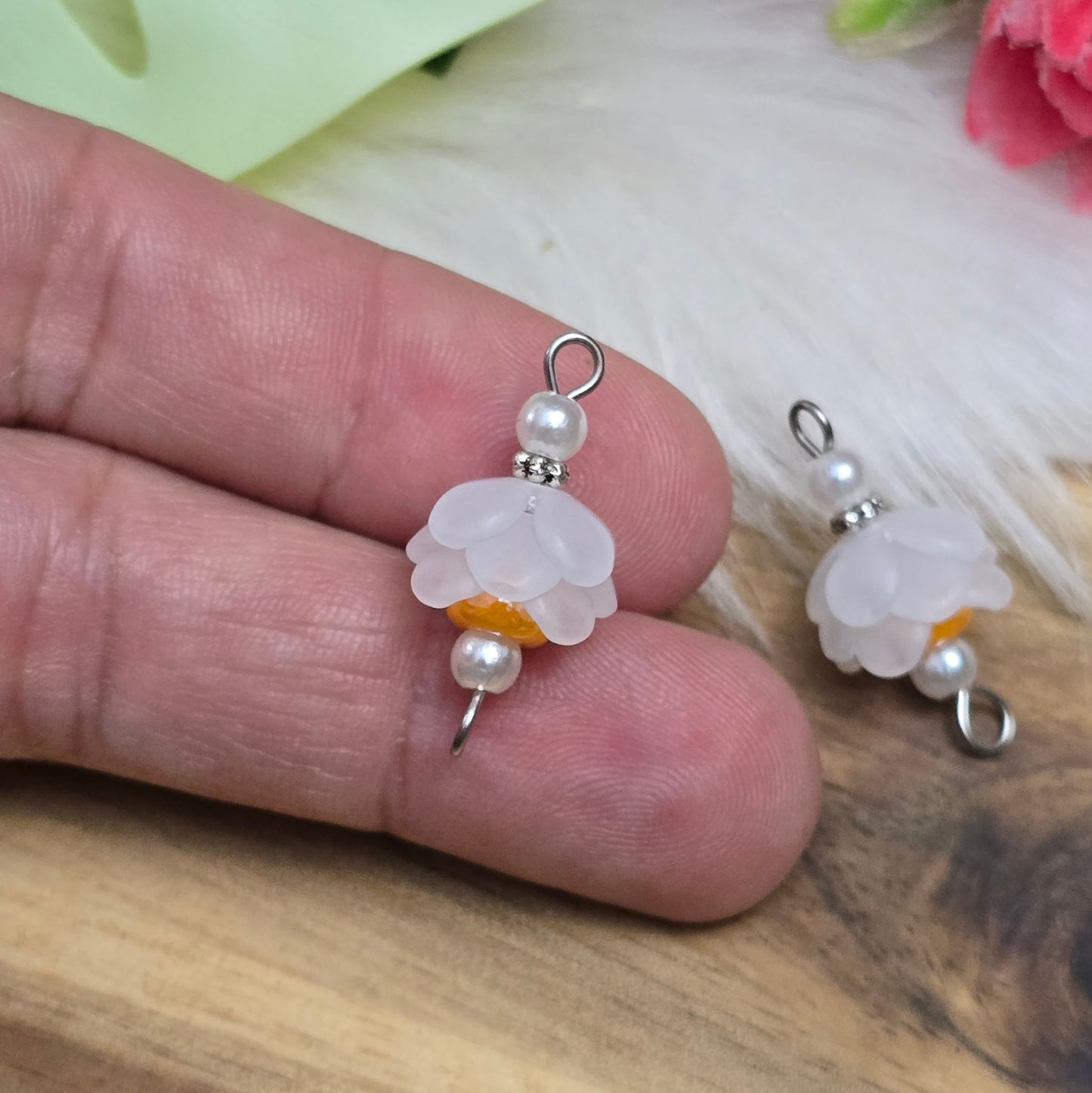 Auf dem Bild sind zwei handgefertigte Blütenverbinder zu sehen. Diese bestehen aus mattierten, weißen Acrylblütenkäppchen, die harmonisch mit cremefarbenen Acrylperlen und leuchtenden, orangen böhmischen Glasperlen kombiniert sind. Die Verbinder haben eine Länge von ca. 24mm und eine Breite von 12mm. Sie sind ideal für kreative Schmuckprojekte und verleihen Armbändern, Halsketten und Ohrringen einen frischen, romantischen Look.