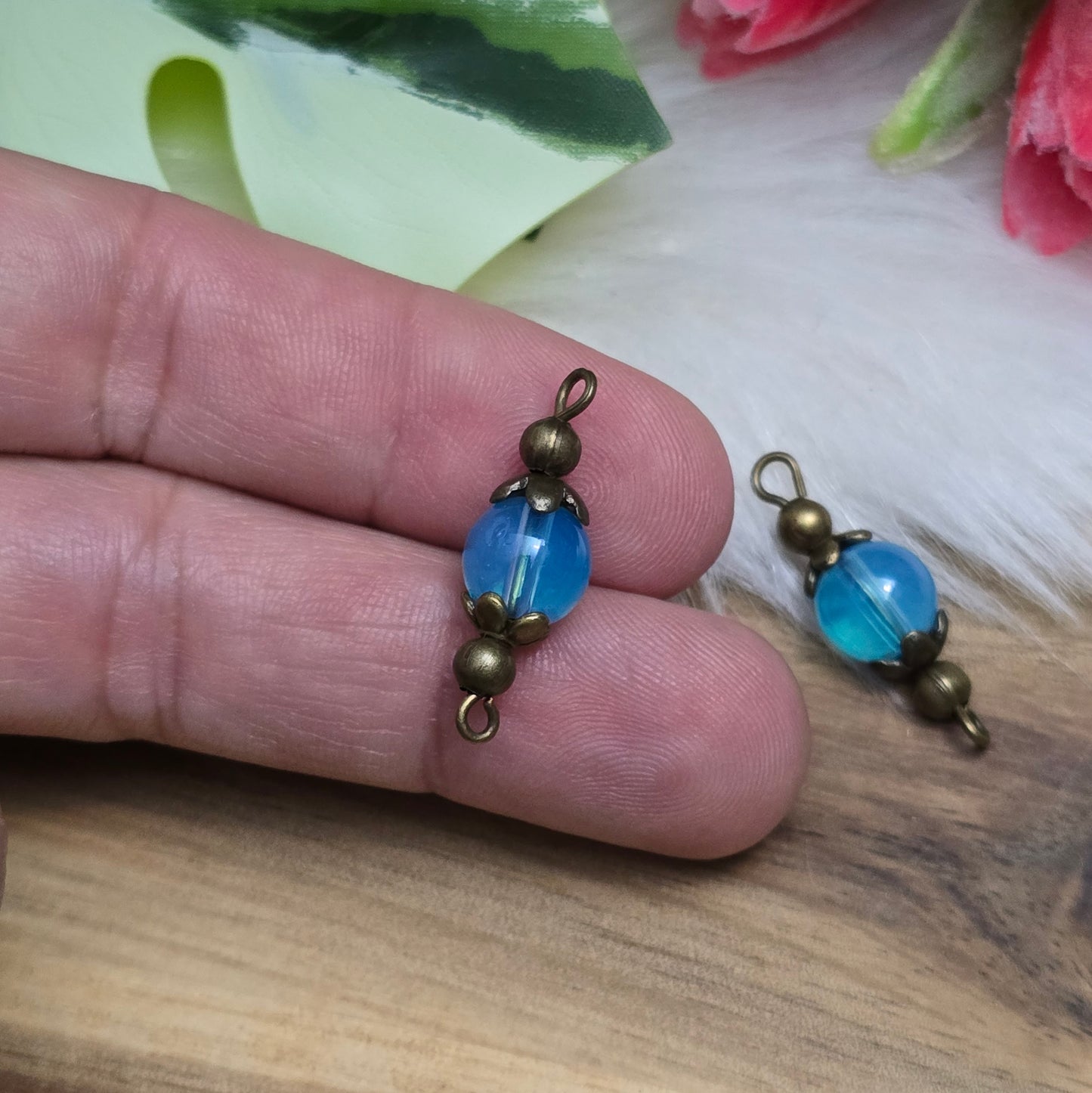 Das Bild zeigt zwei handgefertigte Verbinder mit transparenten, aquablauen Glasperlen, die in antik bronzefarbige Metallelemente eingefasst sind. Die Perlen schimmern sanft und verleihen den Verbindern eine edle Optik. Die filigrane Metallverzierung betont den Vintage-Charakter der Schmuckelemente. Mit einer Länge von ca. 24mm sind sie vielseitig einsetzbar – perfekt für Armbänder, Ketten oder Ohrringe.