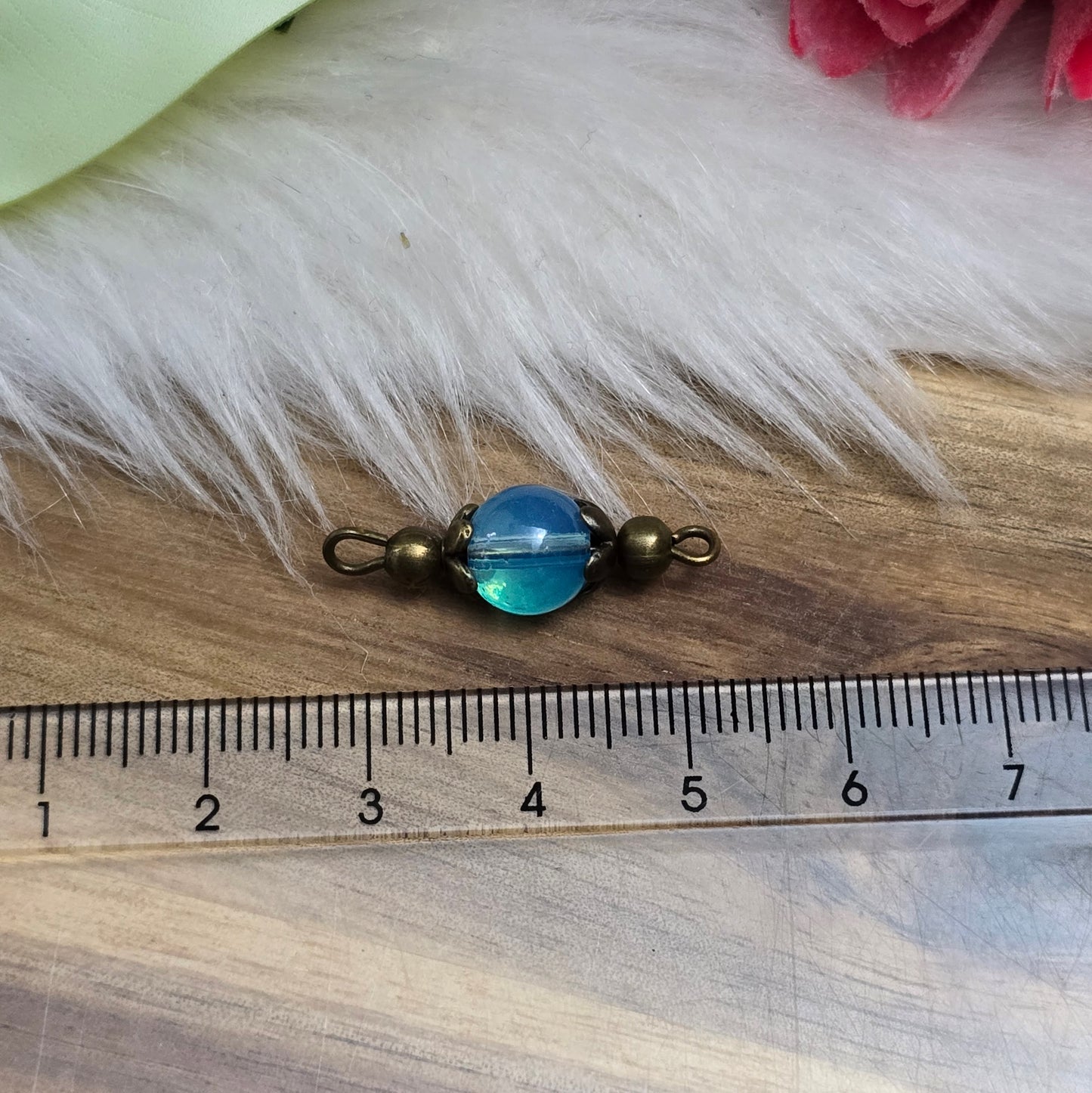 Das Bild zeigt zwei handgefertigte Verbinder mit transparenten, aquablauen Glasperlen, die in antik bronzefarbige Metallelemente eingefasst sind. Die Perlen schimmern sanft und verleihen den Verbindern eine edle Optik. Die filigrane Metallverzierung betont den Vintage-Charakter der Schmuckelemente. Mit einer Länge von ca. 24mm sind sie vielseitig einsetzbar – perfekt für Armbänder, Ketten oder Ohrringe.