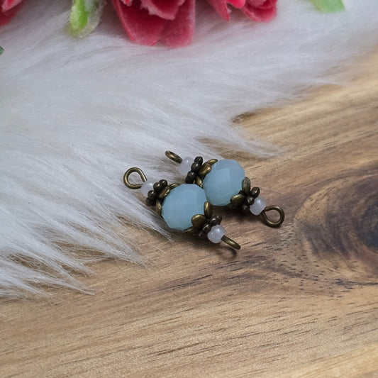 Das Bild zeigt zwei Verbinder mit mintfarbenen Kristallglasperlen und antik bronzefarbigen Metallelementen. Die Verbinder haben eine Länge von 22 mm und präsentieren sich mit einem eleganten, facettierten Design, das das Licht auf funkelnde Weise reflektiert. Die mintfarbenen Glasperlen strahlen eine subtile Frische aus, während die bronzefarbigen Elemente einen warmen, nostalgischen Akzent setzen. Die Kombination aus sanften Farben und hochwertigen Materialien macht diese Verbinder zu einem perfekte