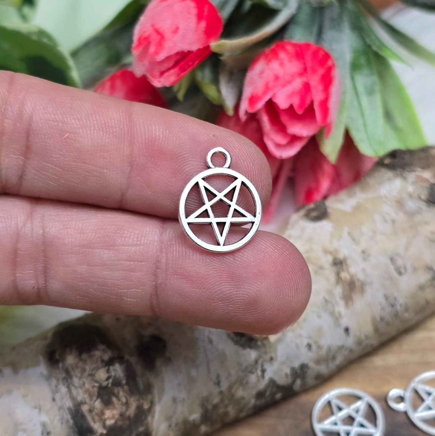 Auf dem Bild sind kleine Anhänger abgebildet, die die Form eines invertierten Pentagramms haben und in antik silberner Farbe gehalten sind. Jeder dieser Anhänger ist in einem Ring eingefasst und misst ungefähr 16 x 13 mm. Die Oberfläche der Anhänger weist eine feine Struktur auf und besitzt eine metallische Beschaffenheit, die das Licht reflektiert und ihnen einen attraktiven Glanz verleiht.