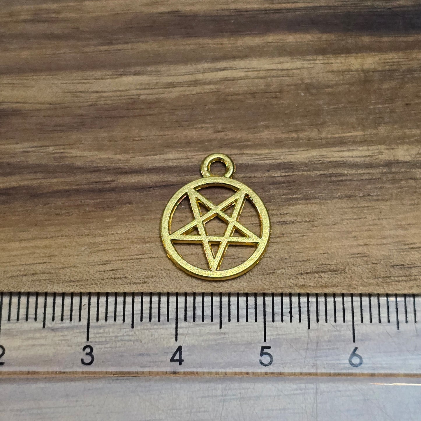 Das Bild zeigt fünf Anhänger in Form eines invertierten Pentagramms, die in vergoldeter Ausführung gestaltet sind. Jeder Anhänger ist in einem geschlossenen Ring gefasst und hat eine Größe von etwa 16 x 13 mm. Die Oberfläche der Anhänger glänzt und reflektiert das Licht, wodurch ein eleganter und ansprechender Effekt entsteht. Die geometrische Form des invertierten Pentagramms vermittelt eine mystische Aura und verleiht den Anhängern einen besonderen Charakter.