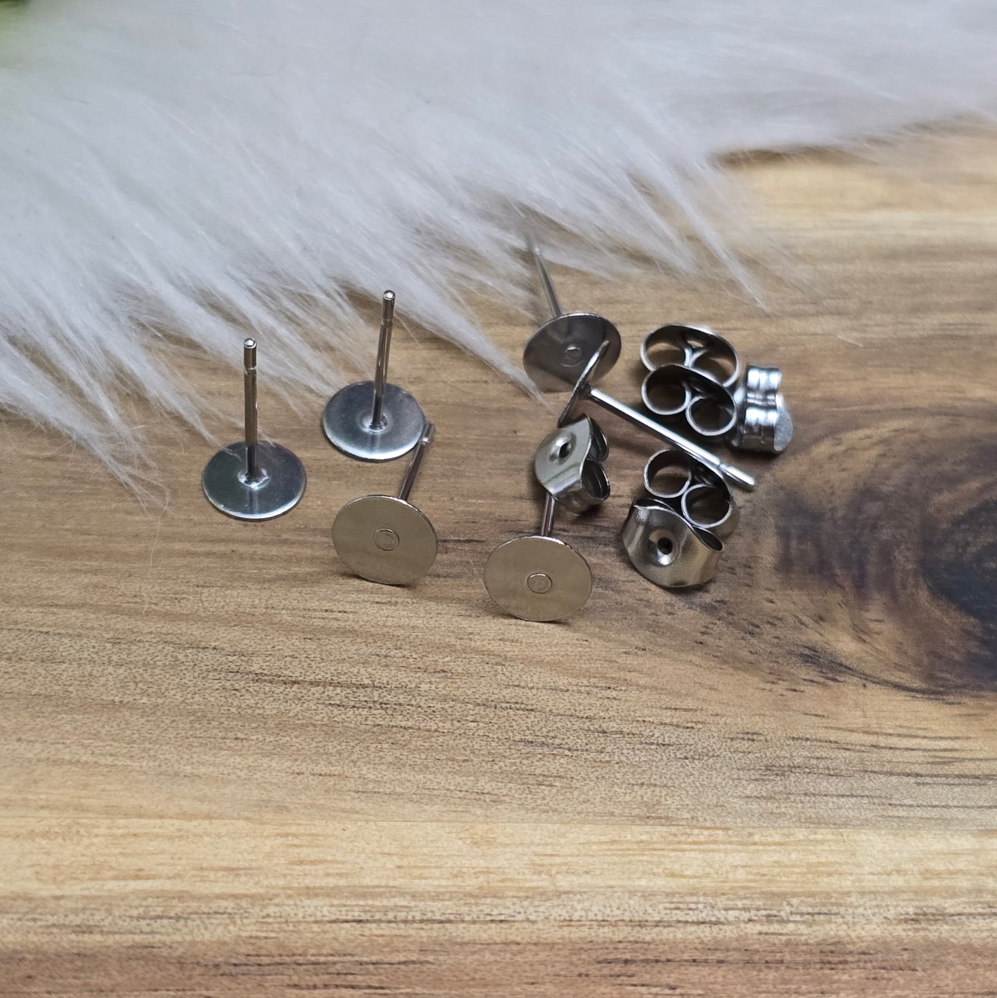 Das Bild zeigt Ohrstecker mit runder Klebeplatte aus Edelstahl in silber mit Flügelmuttern.