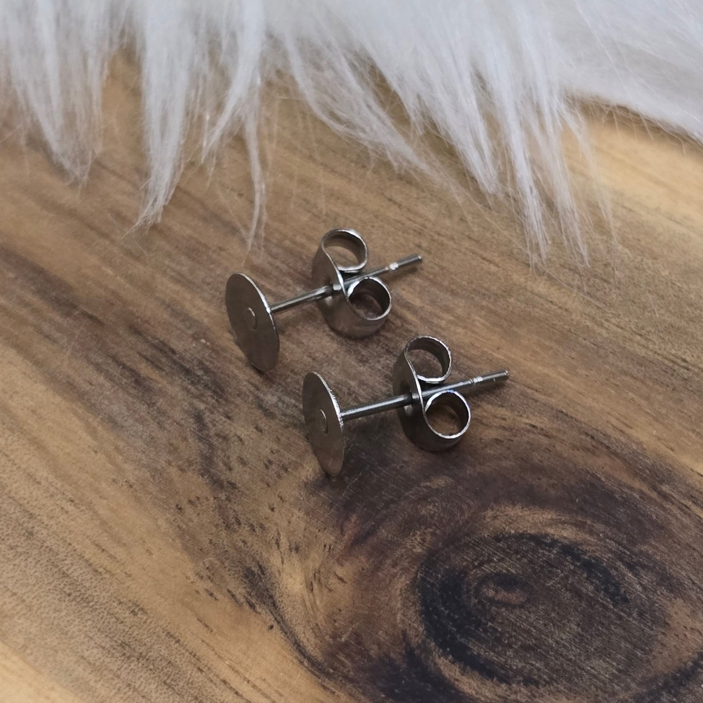 Das Bild zeigt Ohrstecker mit runder Klebeplatte aus Edelstahl in silber mit Flügelmuttern.