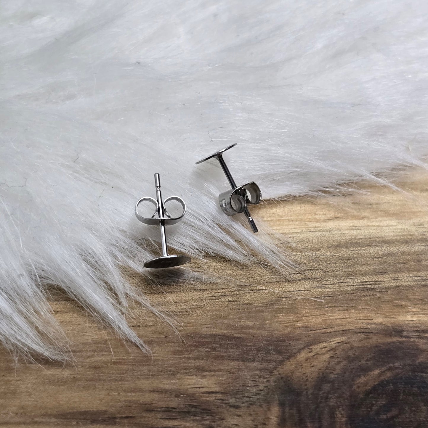 Das Bild zeigt Ohrstecker mit runder Klebeplatte aus Edelstahl in silber mit Flügelmuttern.
