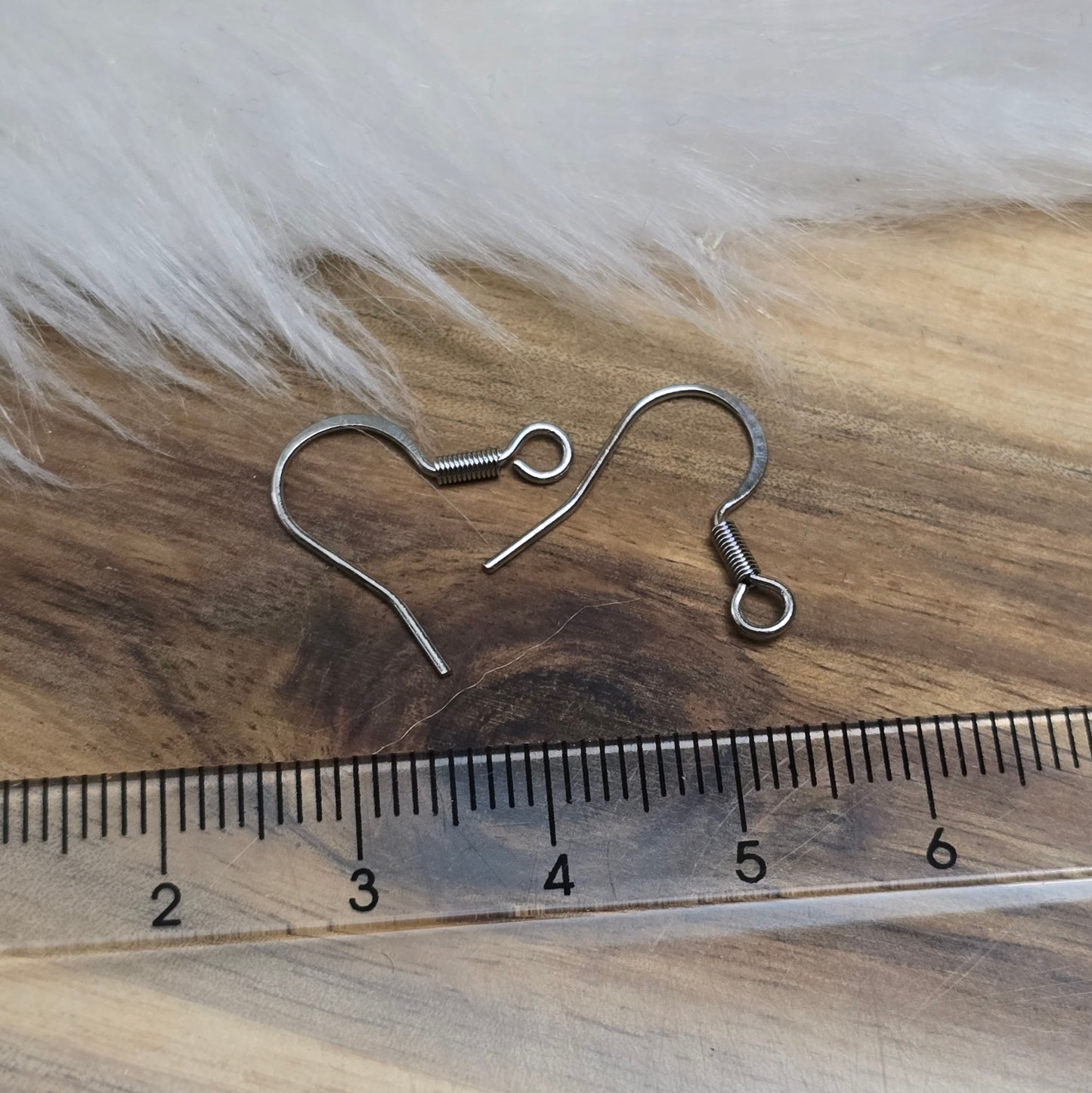 Das Bild zeigt ein Paar French Ohrhaken aus 304 Edelstahl in Silberfarbe. Die Haken haben eine elegante, geschwungene Form mit einer kleinen Öse am unteren Ende, die zur Befestigung von Anhängern oder Perlen dient. Die Oberfläche ist glatt und glänzend, was ihnen ein hochwertiges und modernes Aussehen verleiht. Mit einer Größe von etwa 16 mm sind sie ideal für die Gestaltung individueller Ohrringe.