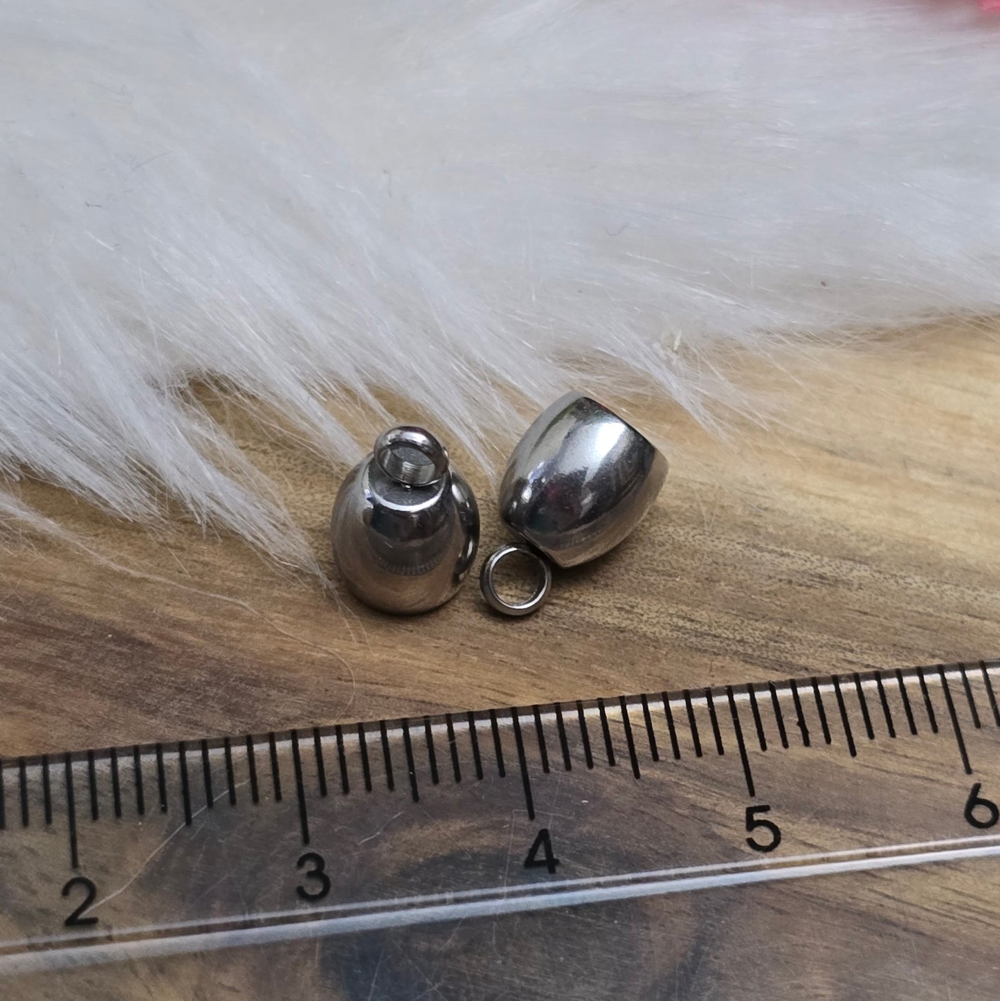 Das Bild zeigt zwei Endkappen aus hochwertigem 304 Edelstahl mit einem Durchmesser von 5 mm. Jede Endkappe verfügt über eine feste Öse, die für einen sicheren Halt sorgt und das Anbringen von Verschlüssen oder Anhängern erleichtert. Die silberfarbene Oberfläche der Endkappen verleiht ihnen ein elegantes und modernes Aussehen. Diese Endkappen sind ideal für die Fertigung von Quasten oder als Abschluss für dicke Bänder aus Materialien wie PU oder Leder, um ein professionelles Finish zu erzielen. Die kompakte