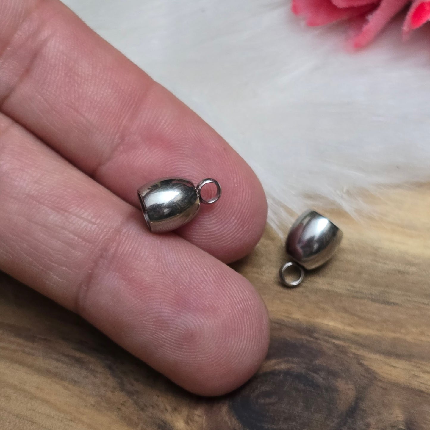 Das Bild zeigt zwei Endkappen aus hochwertigem 304 Edelstahl mit einem Durchmesser von 5 mm. Jede Endkappe verfügt über eine feste Öse, die für einen sicheren Halt sorgt und das Anbringen von Verschlüssen oder Anhängern erleichtert. Die silberfarbene Oberfläche der Endkappen verleiht ihnen ein elegantes und modernes Aussehen. Diese Endkappen sind ideal für die Fertigung von Quasten oder als Abschluss für dicke Bänder aus Materialien wie PU oder Leder, um ein professionelles Finish zu erzielen. Die kompakte