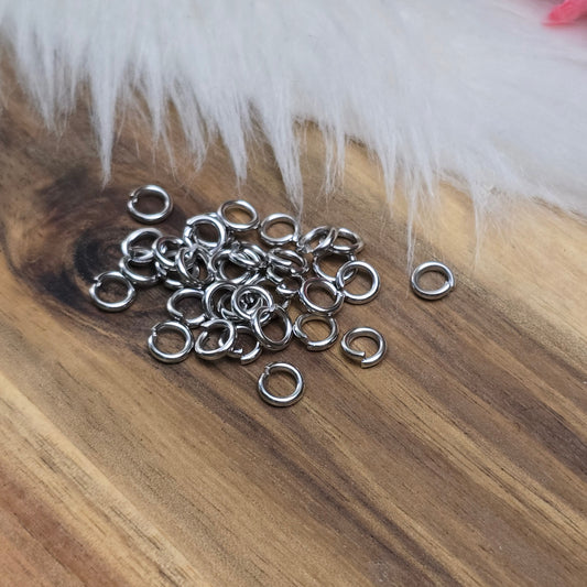 Das Bild zeigt 30 offene Biegeringe aus hochwertigem Edelstahl, die in zwei Größen (Ø 5mm und Ø 6mm) angeordnet sind. Die Biegeringe haben eine glänzende, silberfarbene Oberfläche und sind offen, was ihre einfache Handhabung für das Verbinden von Schmuckkomponenten ermöglicht. Die Ringe sind perfekt für die Herstellung von individuellen Schmuckstücken wie Armbändern, Halsketten oder Ohrringen und bieten eine zuverlässige und langlebige Lösung für kreative Projekte.