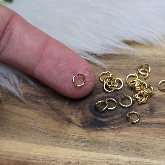 Das Bild zeigt 20 offene Biegeringe aus hochwertigem, vergoldetem Edelstahl mit einem Durchmesser von 5 mm. Die Ringe sind in einem praktischen Set angeordnet und verfügen über eine glänzende goldene Oberfläche, die dem Schmuckdesign einen eleganten Akzent verleiht. Dank des offenen Designs sind die Ringe leicht zu handhaben und ermöglichen eine einfache Verbindung von Schmuckelementen wie Anhängern oder Perlen. Diese Biegeringe sind ideal für die Herstellung individueller Schmuckstücke, darunter Armbänder,