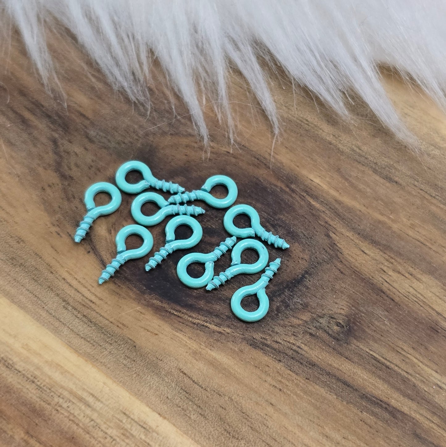 Das Bild zeigt ein Set von 10 farbig lackierten Schraubösen in verschiedenen lebhaften Farben, darunter Hellblau, Grün, Rot, Aqua, Weiß und Rosa. Jede Schrauböse hat die Abmessungen von ca. 8x4mm und ist sorgfältig gestaltet, um eine einfache Anwendung zu ermöglichen. Die Schraubösen sind ideal für das Einschrauben in Materialien wie Holz, Resin oder Acryl, um individuelle Anhänger zu kreieren. Die glänzende Oberfläche der Schraubösen sorgt für einen attraktiven Look, der jedem kreativen Projekt einen farbe