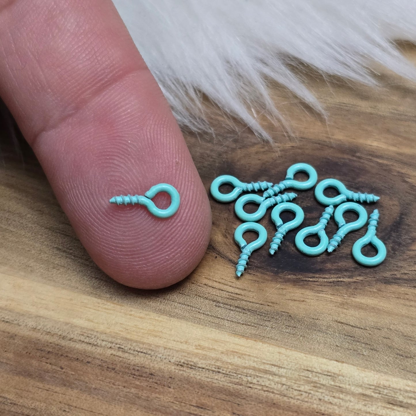 Das Bild zeigt ein Set von 10 farbig lackierten Schraubösen in verschiedenen lebhaften Farben, darunter Hellblau, Grün, Rot, Aqua, Weiß und Rosa. Jede Schrauböse hat die Abmessungen von ca. 8x4mm und ist sorgfältig gestaltet, um eine einfache Anwendung zu ermöglichen. Die Schraubösen sind ideal für das Einschrauben in Materialien wie Holz, Resin oder Acryl, um individuelle Anhänger zu kreieren. Die glänzende Oberfläche der Schraubösen sorgt für einen attraktiven Look, der jedem kreativen Projekt einen farbe