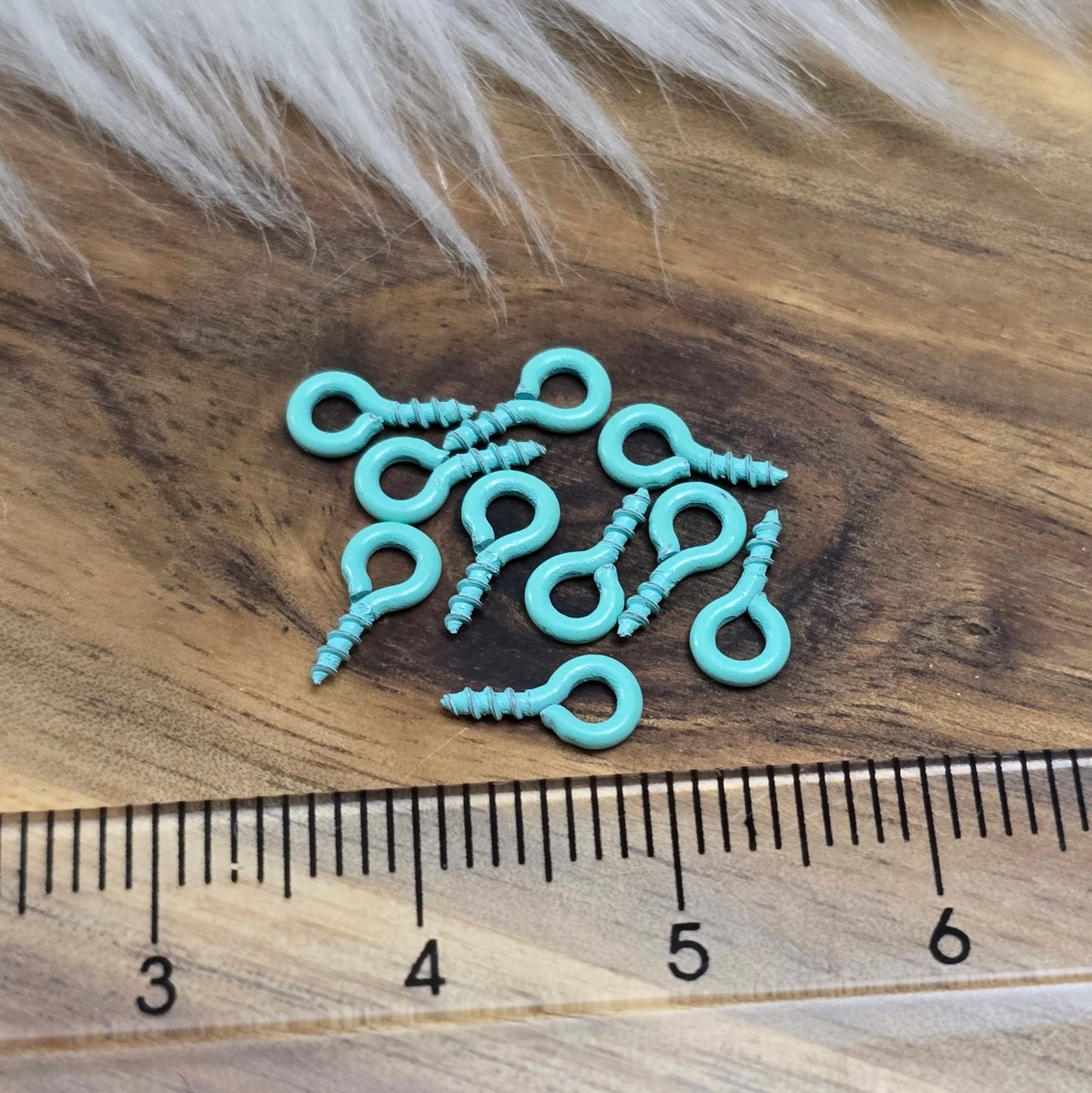 Das Bild zeigt ein Set von 10 farbig lackierten Schraubösen in verschiedenen lebhaften Farben, darunter Hellblau, Grün, Rot, Aqua, Weiß und Rosa. Jede Schrauböse hat die Abmessungen von ca. 8x4mm und ist sorgfältig gestaltet, um eine einfache Anwendung zu ermöglichen. Die Schraubösen sind ideal für das Einschrauben in Materialien wie Holz, Resin oder Acryl, um individuelle Anhänger zu kreieren. Die glänzende Oberfläche der Schraubösen sorgt für einen attraktiven Look, der jedem kreativen Projekt einen farbe