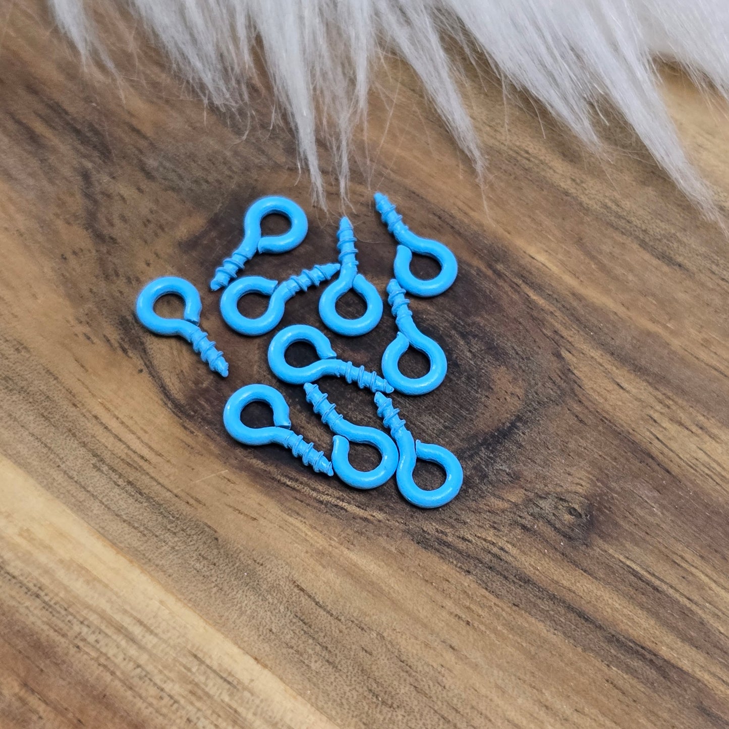Das Bild zeigt ein Set von 10 farbig lackierten Schraubösen in verschiedenen lebhaften Farben, darunter Hellblau, Grün, Rot, Aqua, Weiß und Rosa. Jede Schrauböse hat die Abmessungen von ca. 8x4mm und ist sorgfältig gestaltet, um eine einfache Anwendung zu ermöglichen. Die Schraubösen sind ideal für das Einschrauben in Materialien wie Holz, Resin oder Acryl, um individuelle Anhänger zu kreieren. Die glänzende Oberfläche der Schraubösen sorgt für einen attraktiven Look, der jedem kreativen Projekt einen farbe