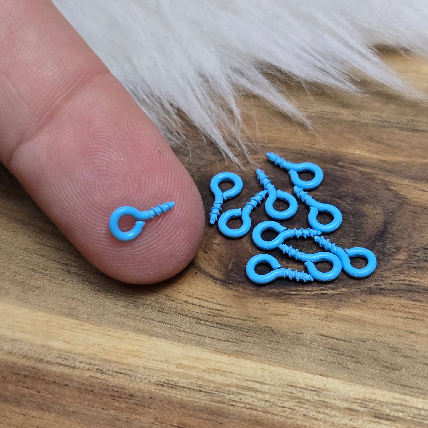 Das Bild zeigt ein Set von 10 farbig lackierten Schraubösen in verschiedenen lebhaften Farben, darunter Hellblau, Grün, Rot, Aqua, Weiß und Rosa. Jede Schrauböse hat die Abmessungen von ca. 8x4mm und ist sorgfältig gestaltet, um eine einfache Anwendung zu ermöglichen. Die Schraubösen sind ideal für das Einschrauben in Materialien wie Holz, Resin oder Acryl, um individuelle Anhänger zu kreieren. Die glänzende Oberfläche der Schraubösen sorgt für einen attraktiven Look, der jedem kreativen Projekt einen farbe