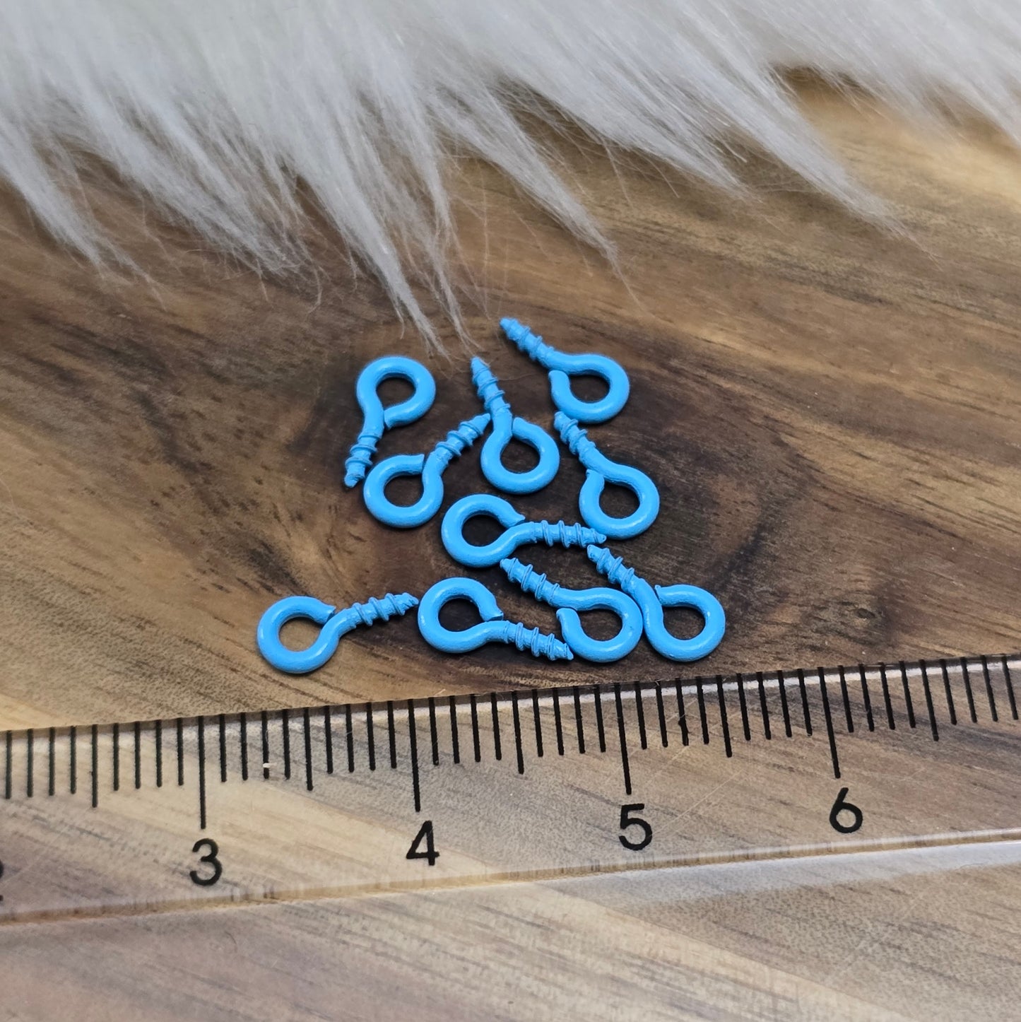 Das Bild zeigt ein Set von 10 farbig lackierten Schraubösen in verschiedenen lebhaften Farben, darunter Hellblau, Grün, Rot, Aqua, Weiß und Rosa. Jede Schrauböse hat die Abmessungen von ca. 8x4mm und ist sorgfältig gestaltet, um eine einfache Anwendung zu ermöglichen. Die Schraubösen sind ideal für das Einschrauben in Materialien wie Holz, Resin oder Acryl, um individuelle Anhänger zu kreieren. Die glänzende Oberfläche der Schraubösen sorgt für einen attraktiven Look, der jedem kreativen Projekt einen farbe