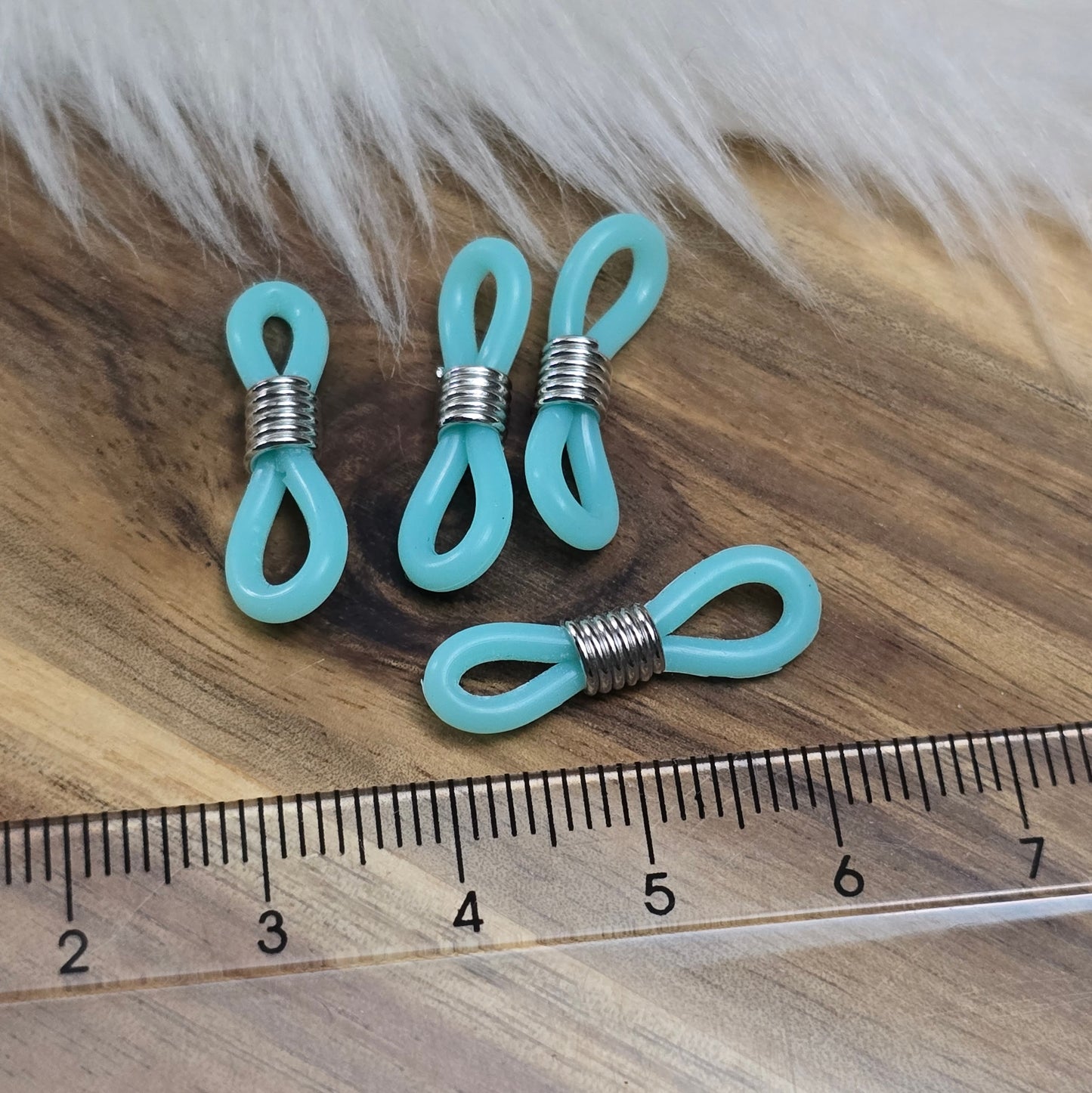 Das Bild zeigt eine Auswahl an Silikonschlaufen für Brillenketten und Maskenhalter in drei Farben: Mint, Rosa und Schwarz. Jede Schlaufe hat eine flexible, weiche Textur und ist so gestaltet, dass sie einfach auf den Bügel der Brille geschoben werden kann. An einem Ende der Schlaufe befindet sich ein kleiner Metallring, der fest angebracht ist, um ein Abrutschen zu verhindern. Die anderen Enden der Schlaufen sind offen, sodass sie mit einem Karabiner oder Biegering leicht an einer Kette befestigt werden kön