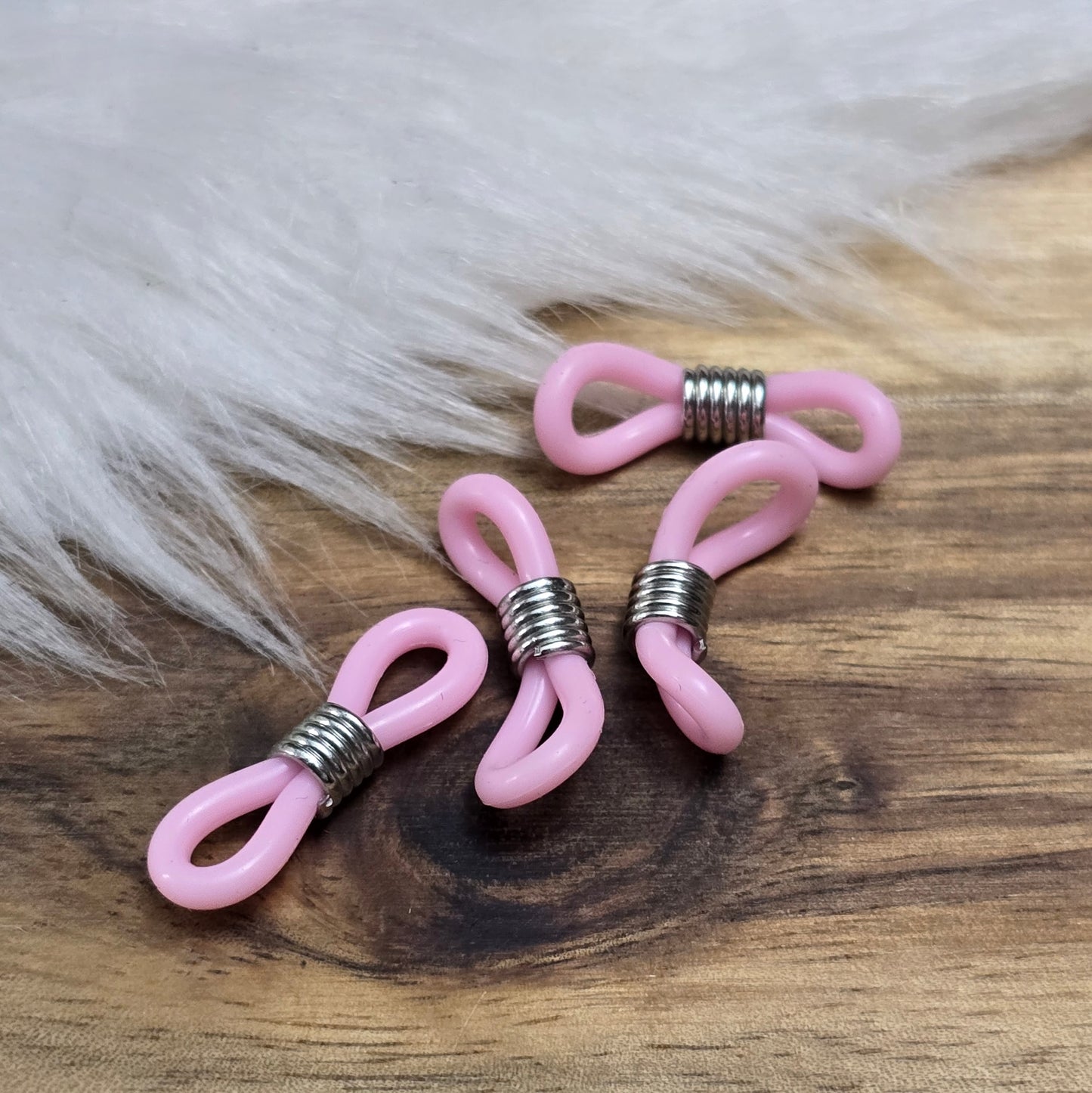 Das Bild zeigt eine Auswahl an Silikonschlaufen für Brillenketten und Maskenhalter in drei Farben: Mint, Rosa und Schwarz. Jede Schlaufe hat eine flexible, weiche Textur und ist so gestaltet, dass sie einfach auf den Bügel der Brille geschoben werden kann. An einem Ende der Schlaufe befindet sich ein kleiner Metallring, der fest angebracht ist, um ein Abrutschen zu verhindern. Die anderen Enden der Schlaufen sind offen, sodass sie mit einem Karabiner oder Biegering leicht an einer Kette befestigt werden kön